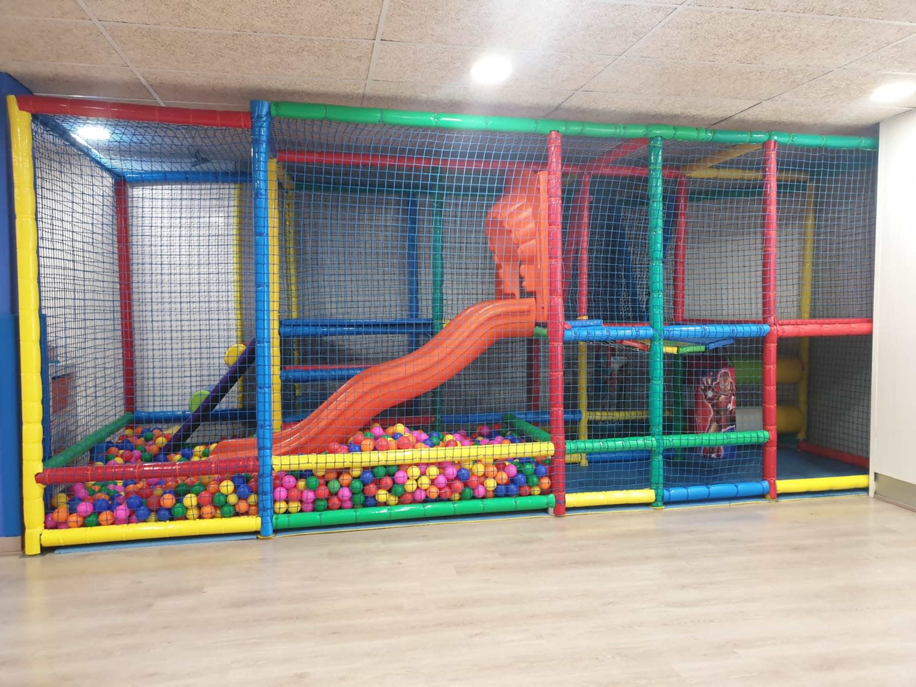 An indoor play structure with a large orange slide, colorful ball pit, and netted barriers for safety.