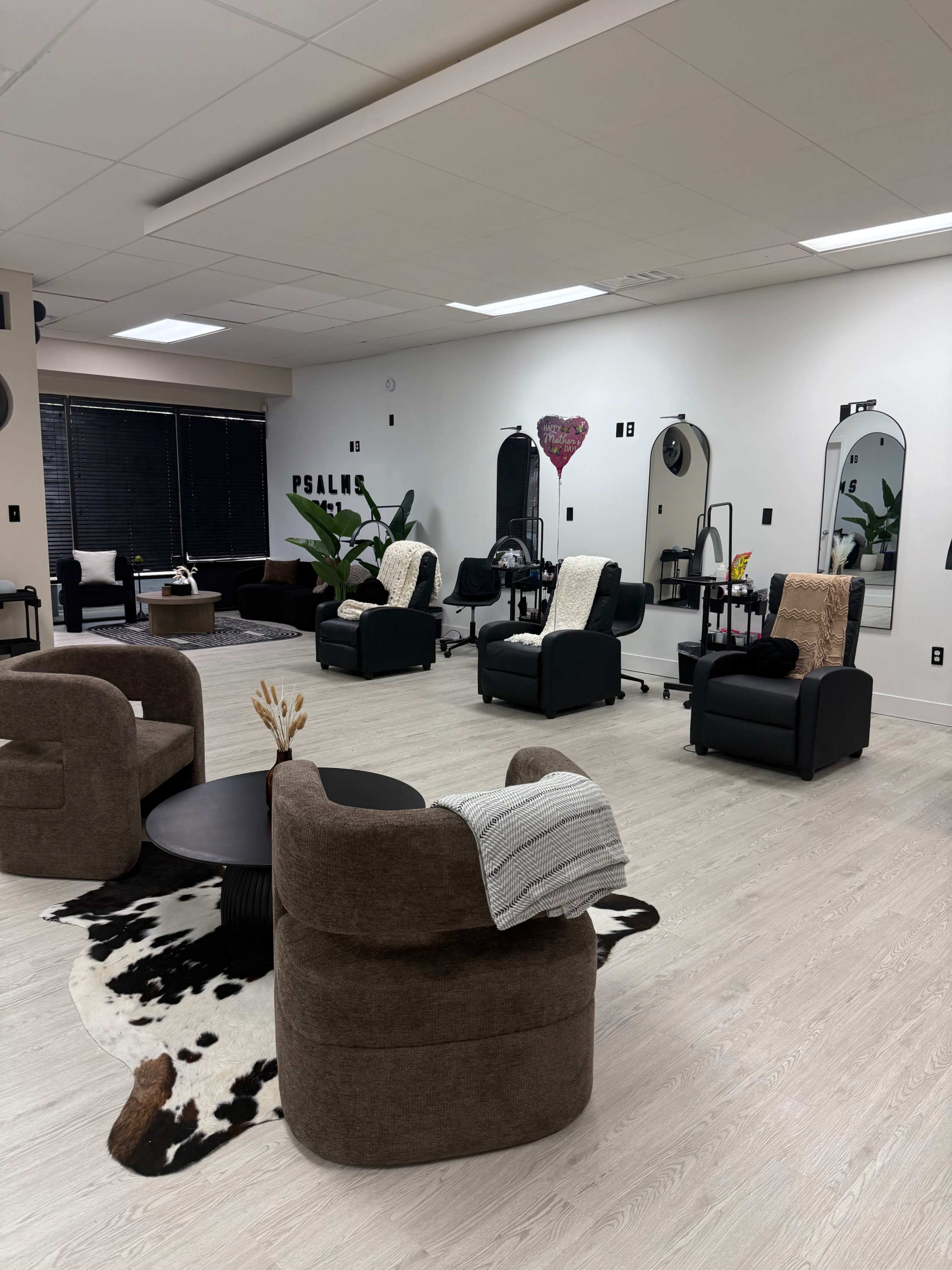 The image shows a modern, spacious salon with several seating areas, mirrors, and plants, arranged around a central coffee table.