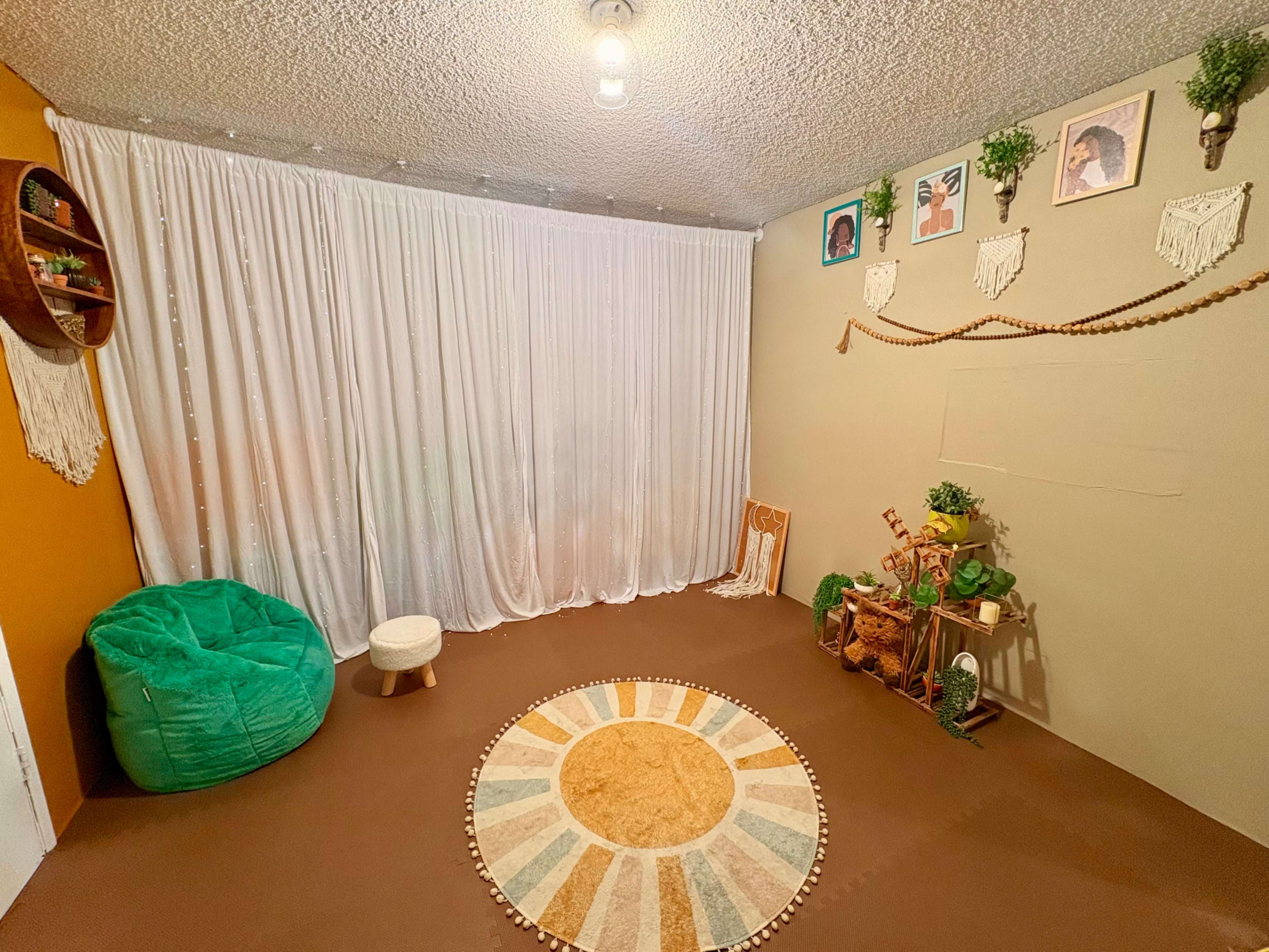 The image shows a cozy indoor space featuring a circular rug, a green bean bag chair, and decorative elements like plants and wall hangings.