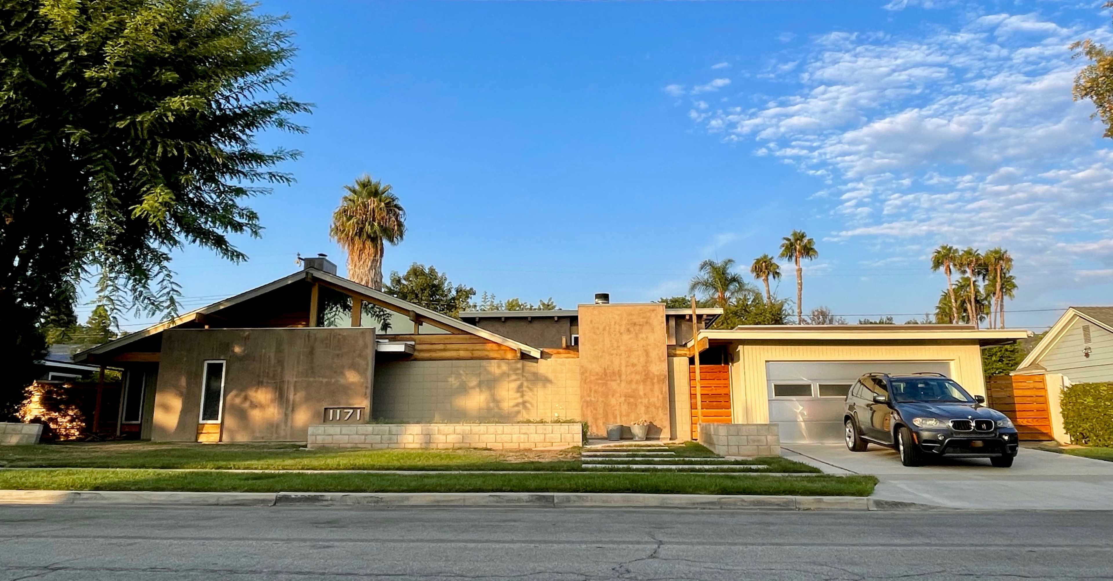 A modern single-story house with a flat roof, concrete and wood siding, and a gray car parked in the driveway.