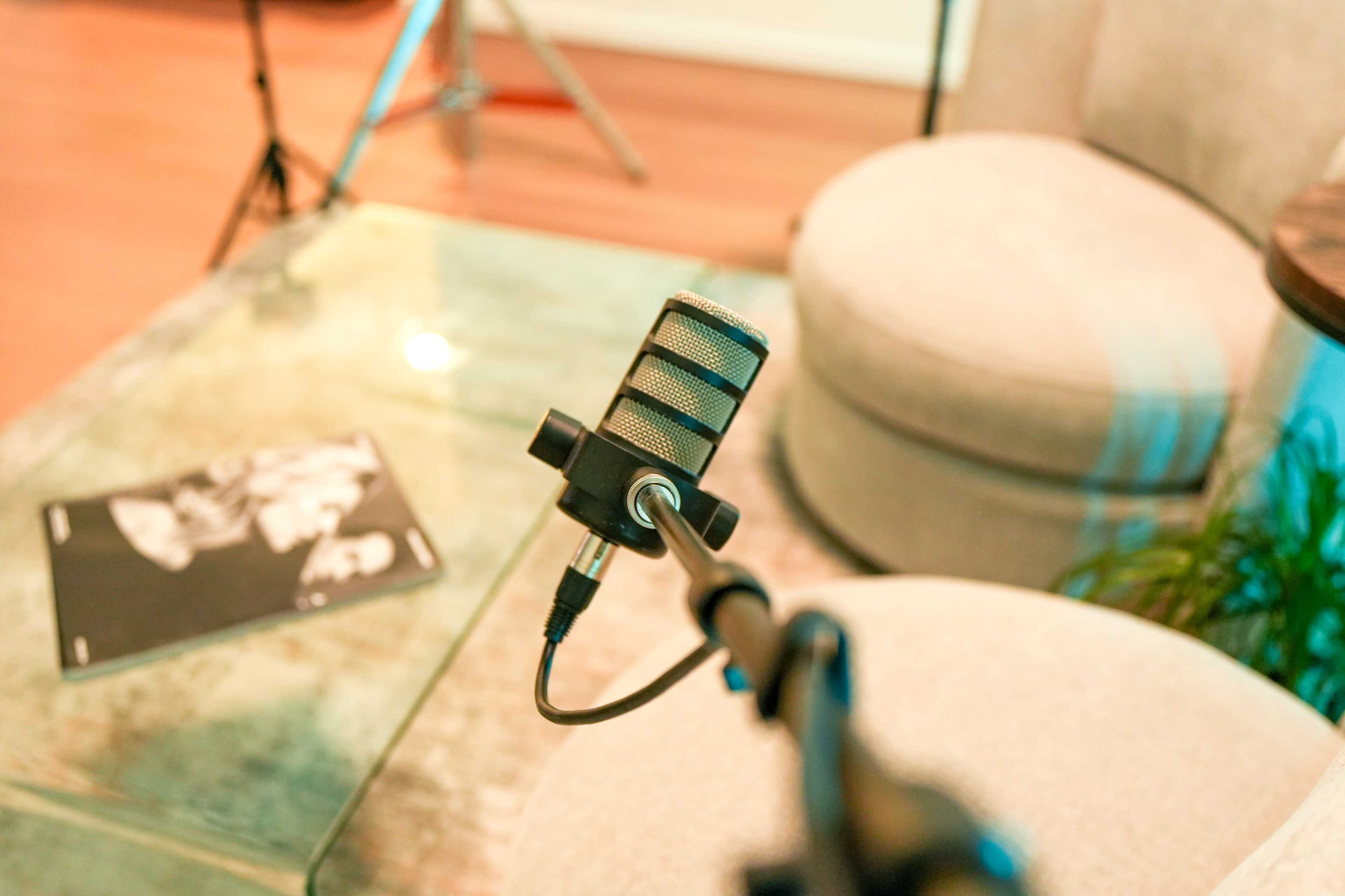 A microphone stands on a table next to a magazine and a pair of empty chairs in a cozy room setting.