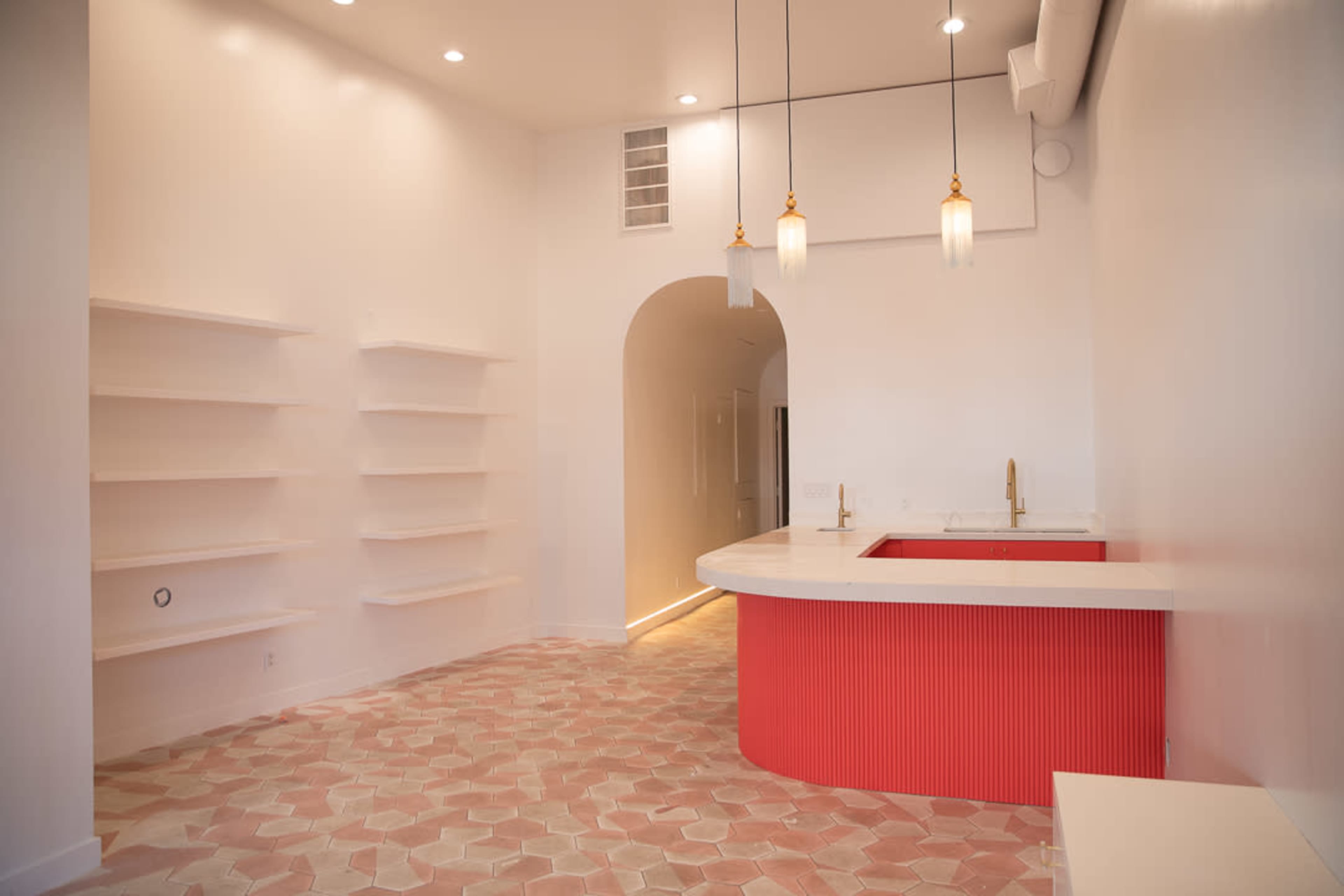 A modern interior space featuring a curved counter with a red accent, light-colored walls, and hexagonal tiled flooring.