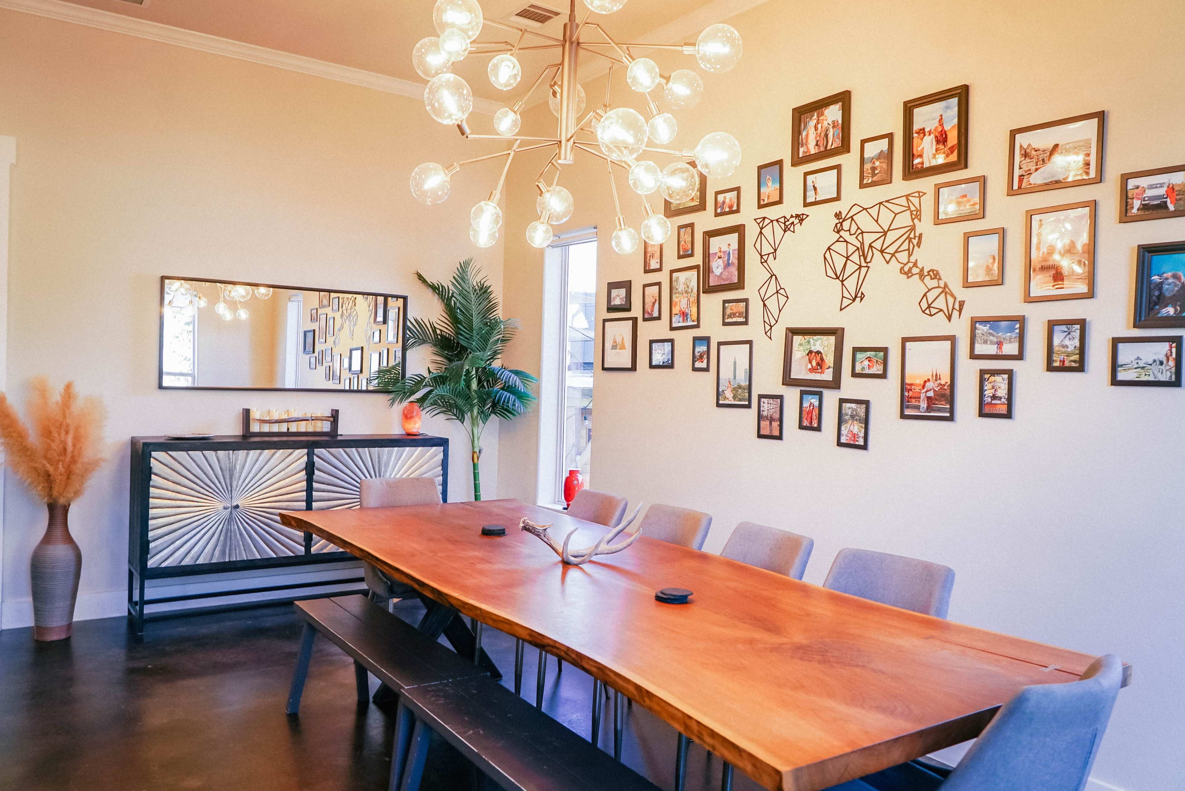 A dining area features a large wooden table surrounded by gray chairs, with a gallery wall of framed photos and a modern light fixture above.