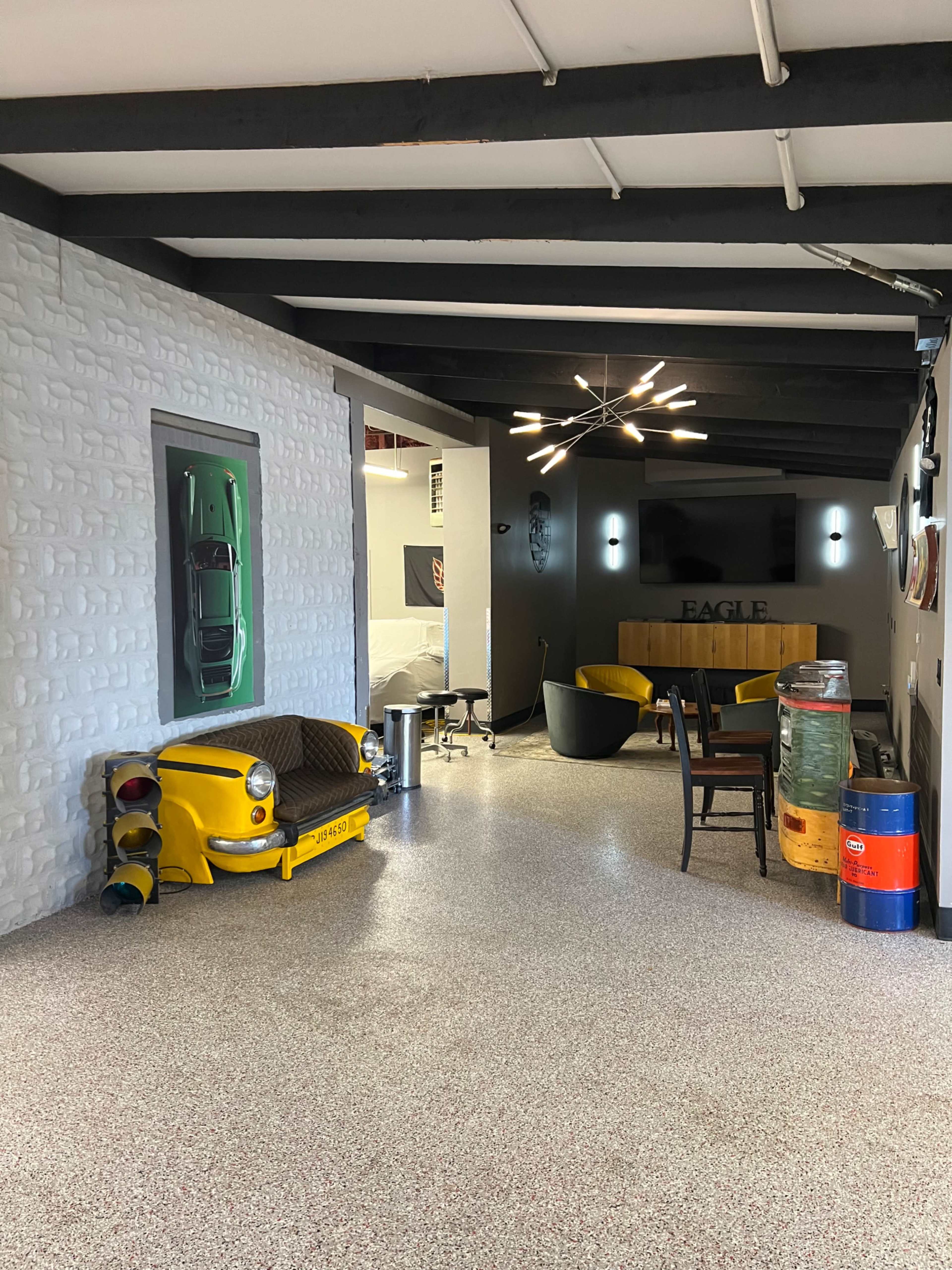 A modern, industrial-style lounge area featuring a yellow taxi-themed couch, a black chair, and a wall-mounted television.