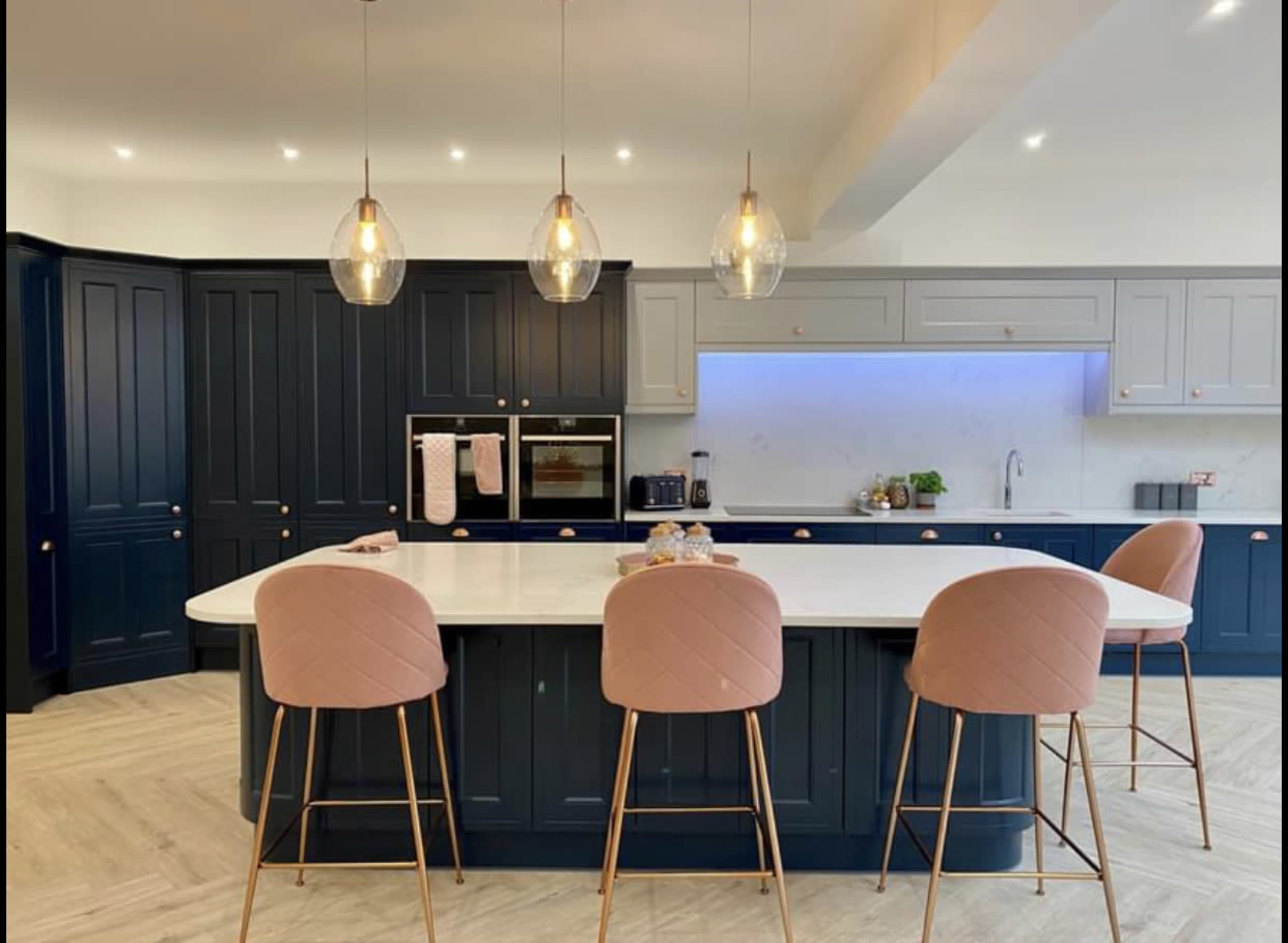 The kitchen features a large island with four bar stools, surrounded by dark blue cabinetry and modern pendant lights.
