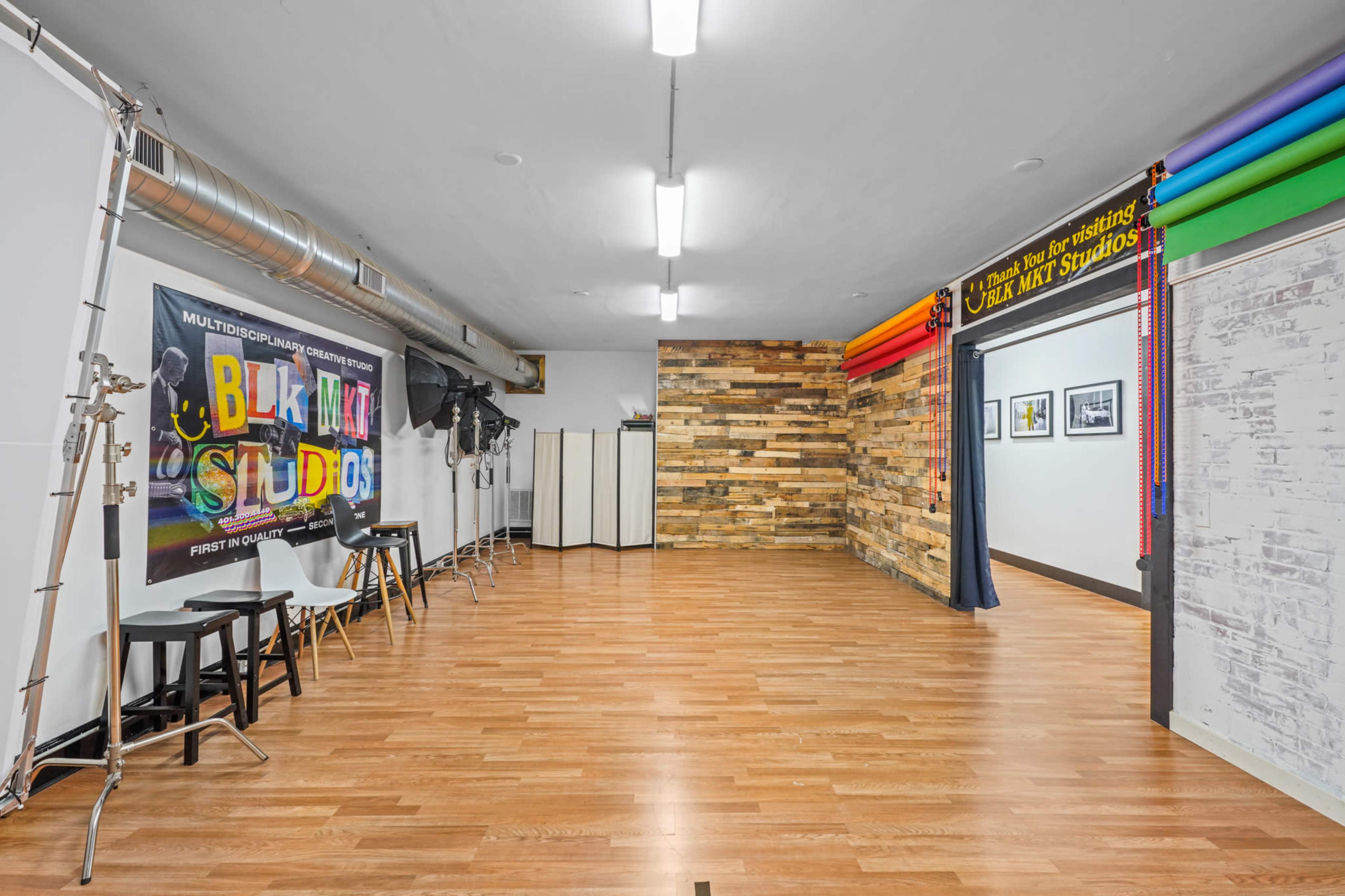 An interior studio space featuring wooden flooring, colorful backdrops on one wall, and equipment stands along with photography studio elements.