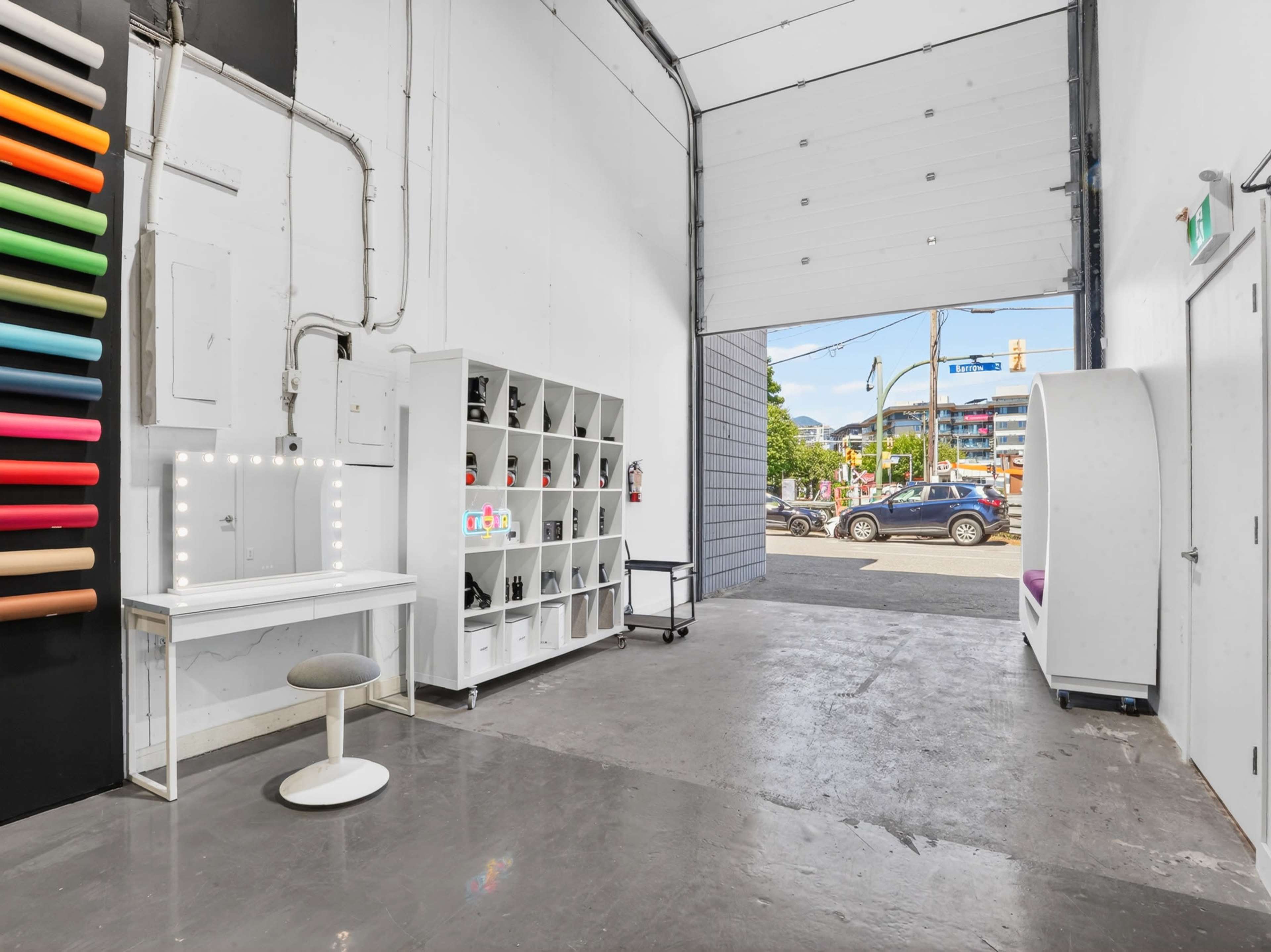 The image shows an interior space featuring a white makeup vanity, storage shelves, and an open doorway leading to a street view.