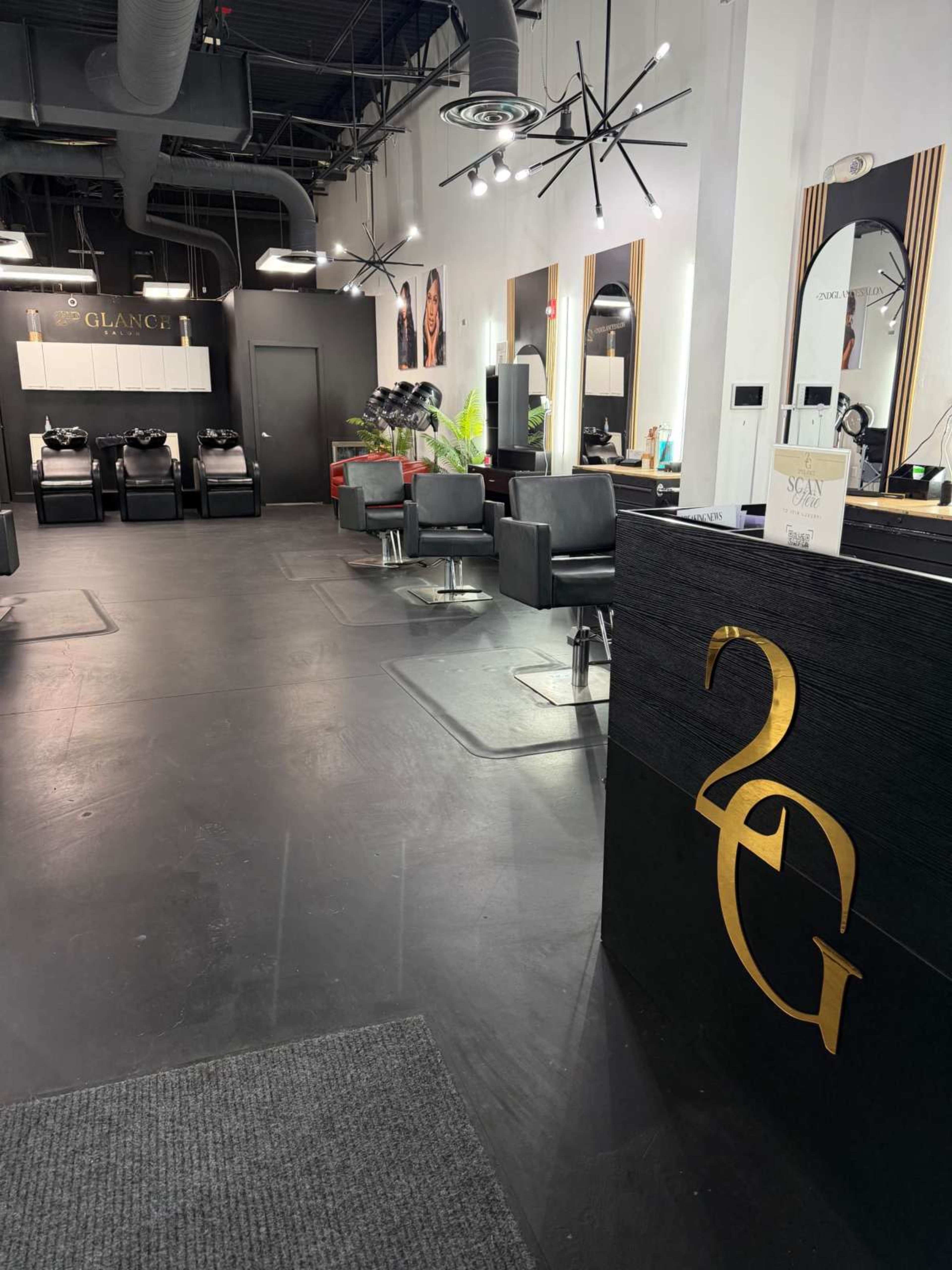 The image shows a modern hair salon interior featuring sleek black furniture, salon chairs, and a reception desk with the logo "2G" prominently displayed.