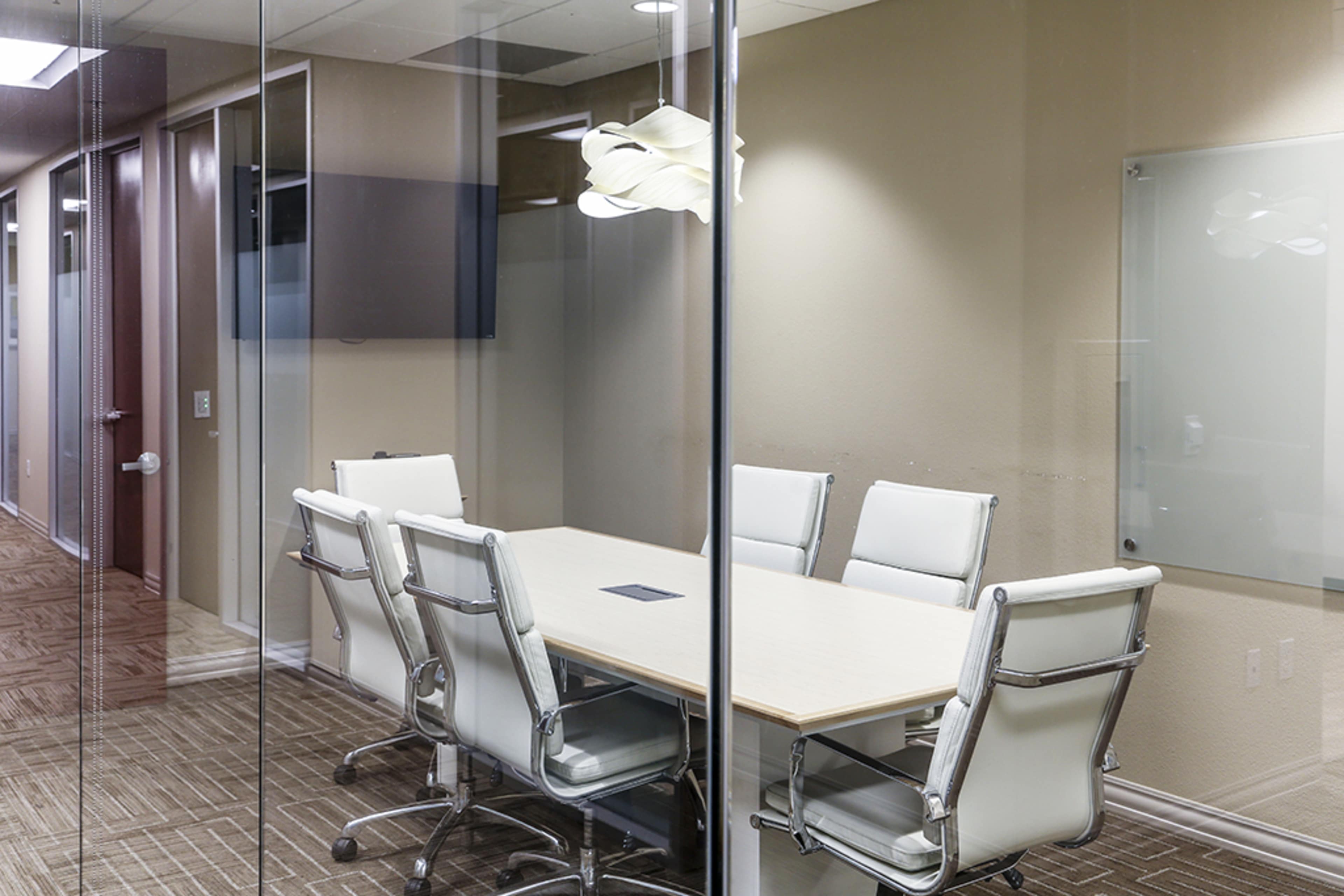 A modern conference room with a long table and several white leather chairs surrounded by glass walls.