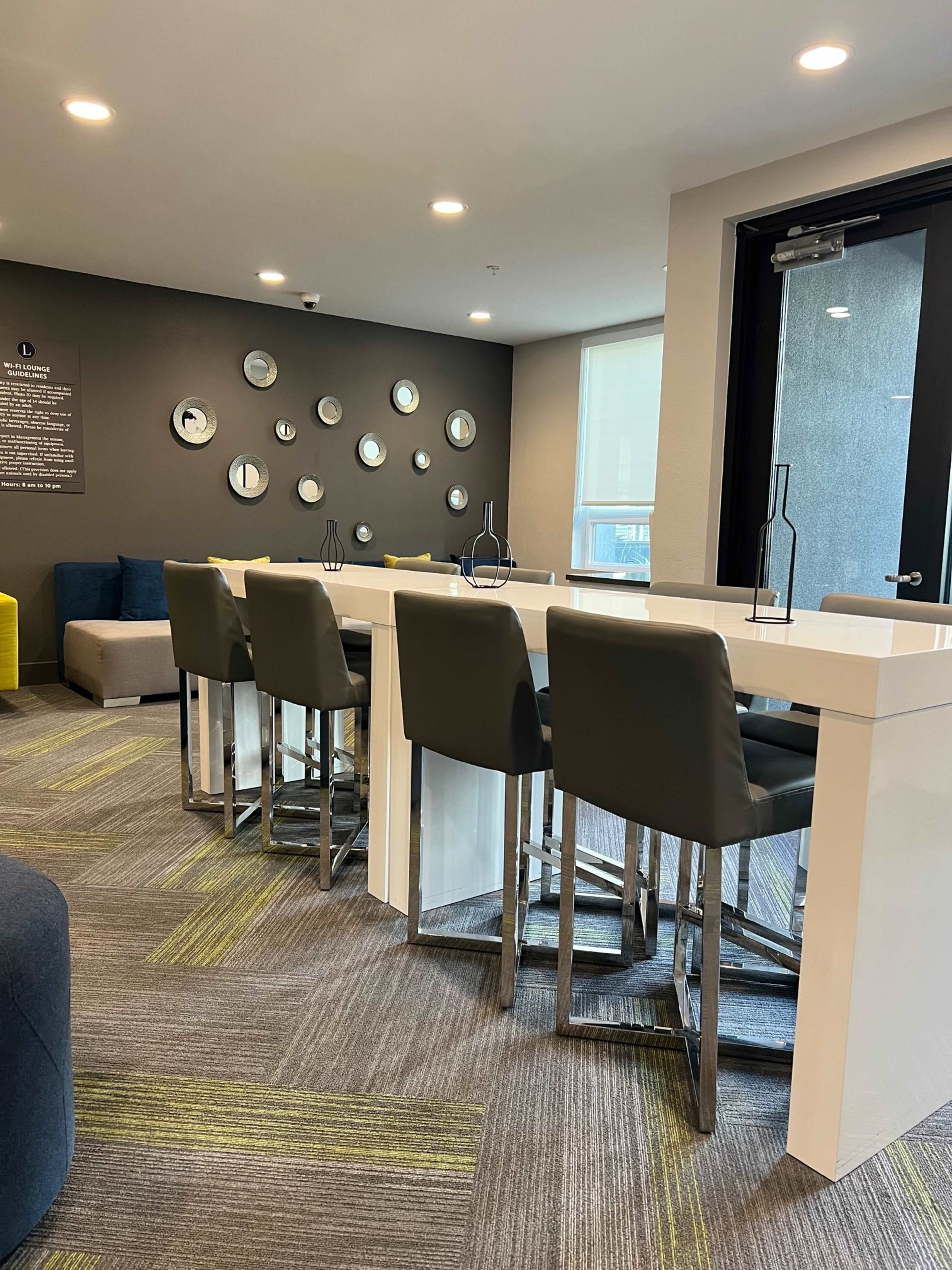 The image shows a modern lounge area featuring a row of high-backed chairs at a white counter, with circular mirrors on the wall.