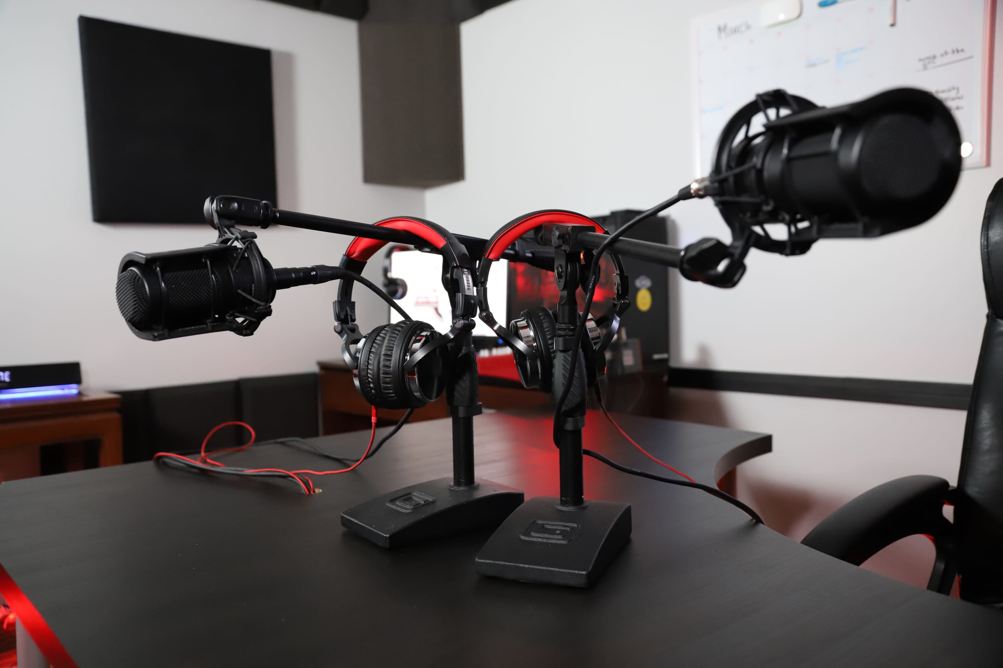 The image shows two microphones mounted on stands with headphones hanging from each, set on a black table in a recording studio.