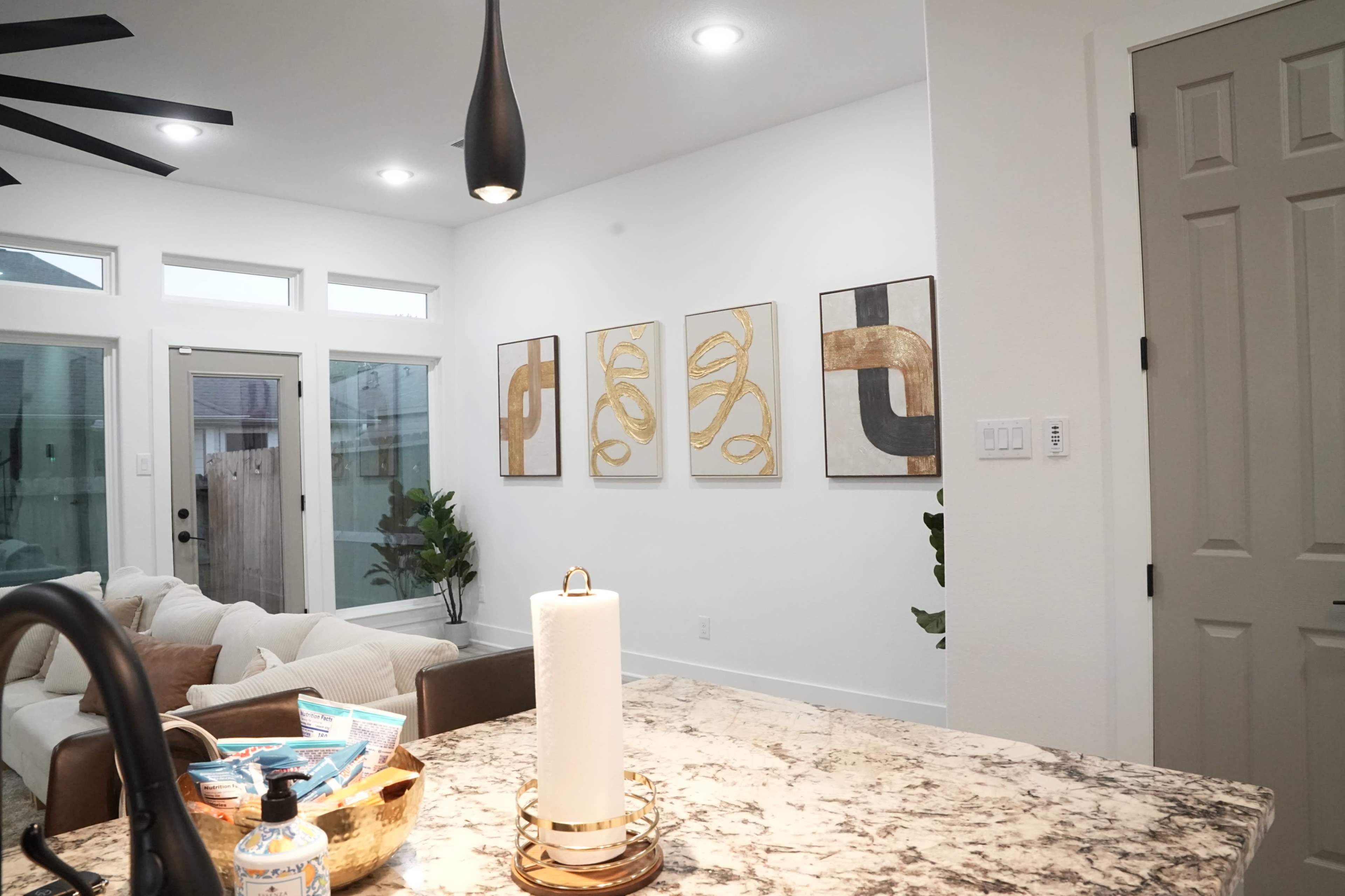 The image shows a modern interior space with abstract artwork on the wall, a kitchen area in the foreground, and a living room area visible in the background.