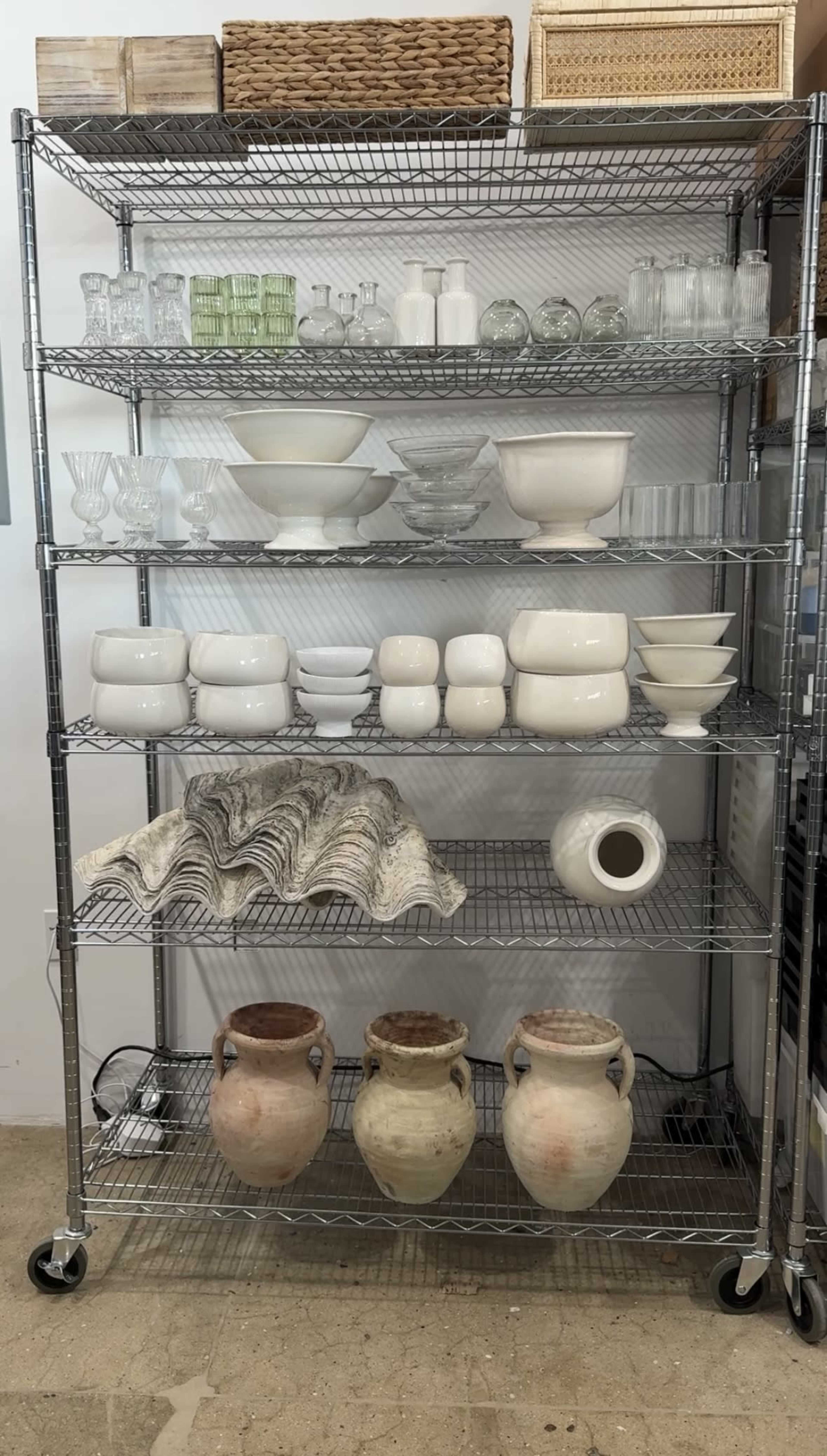A metal shelving unit displays various glass and ceramic containers, including bowls, vases, and decorative items, arranged across six shelves.
