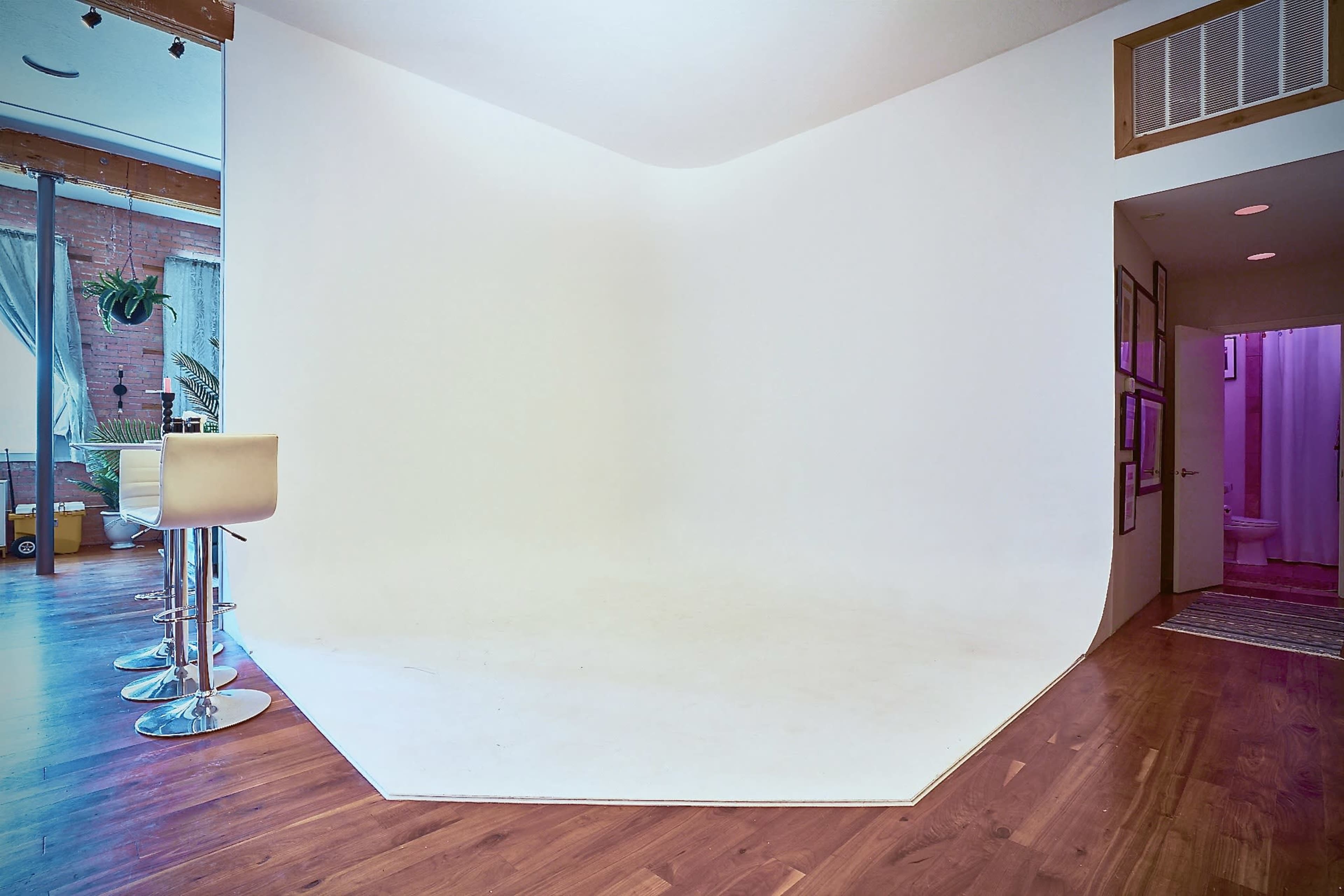 A spacious, empty room featuring a white, hexagonal backdrop and hardwood flooring, with a bar stool positioned in front.