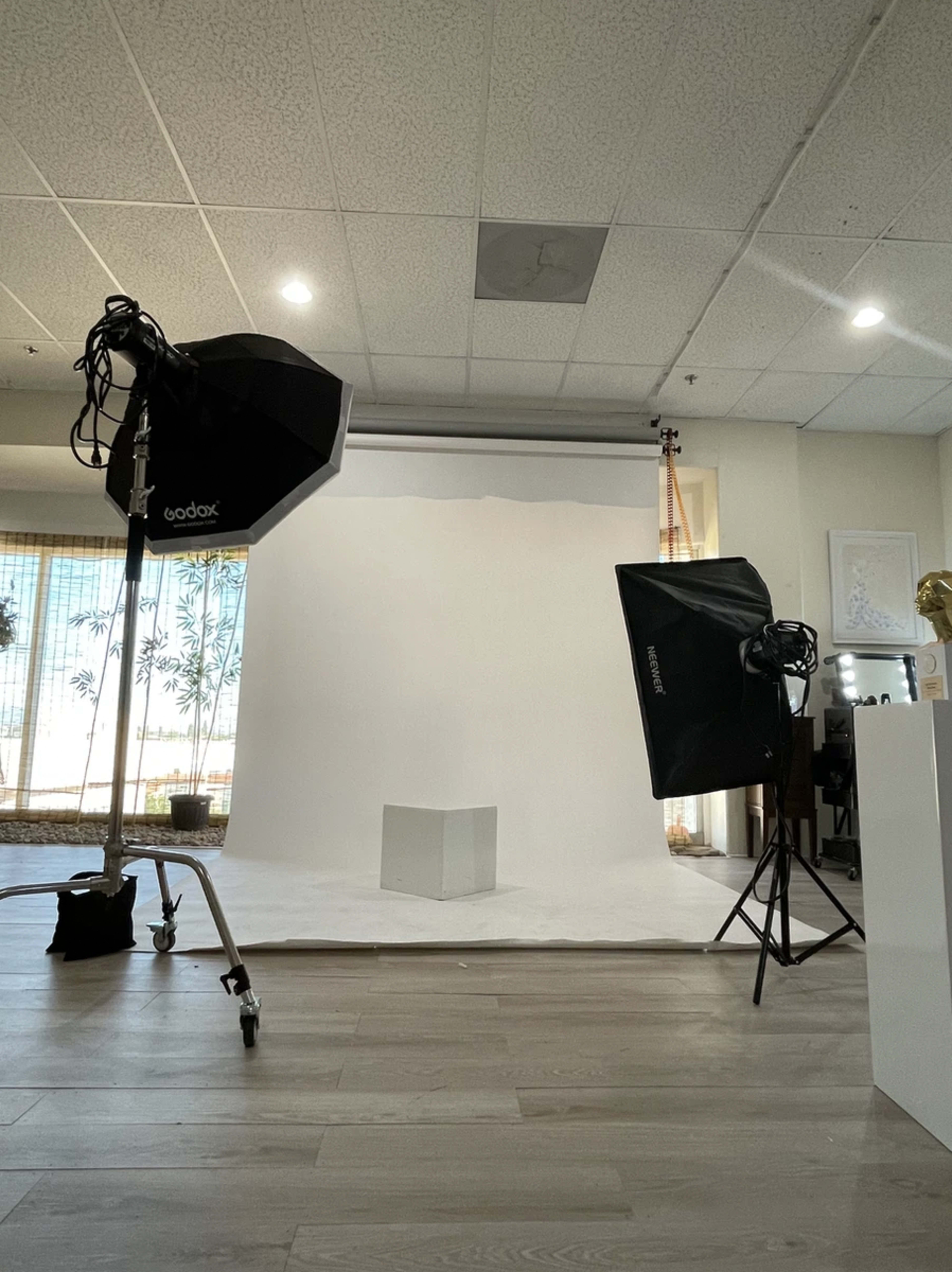 A photography studio setup with two lights, a white backdrop, and a clear cube placed on the floor.