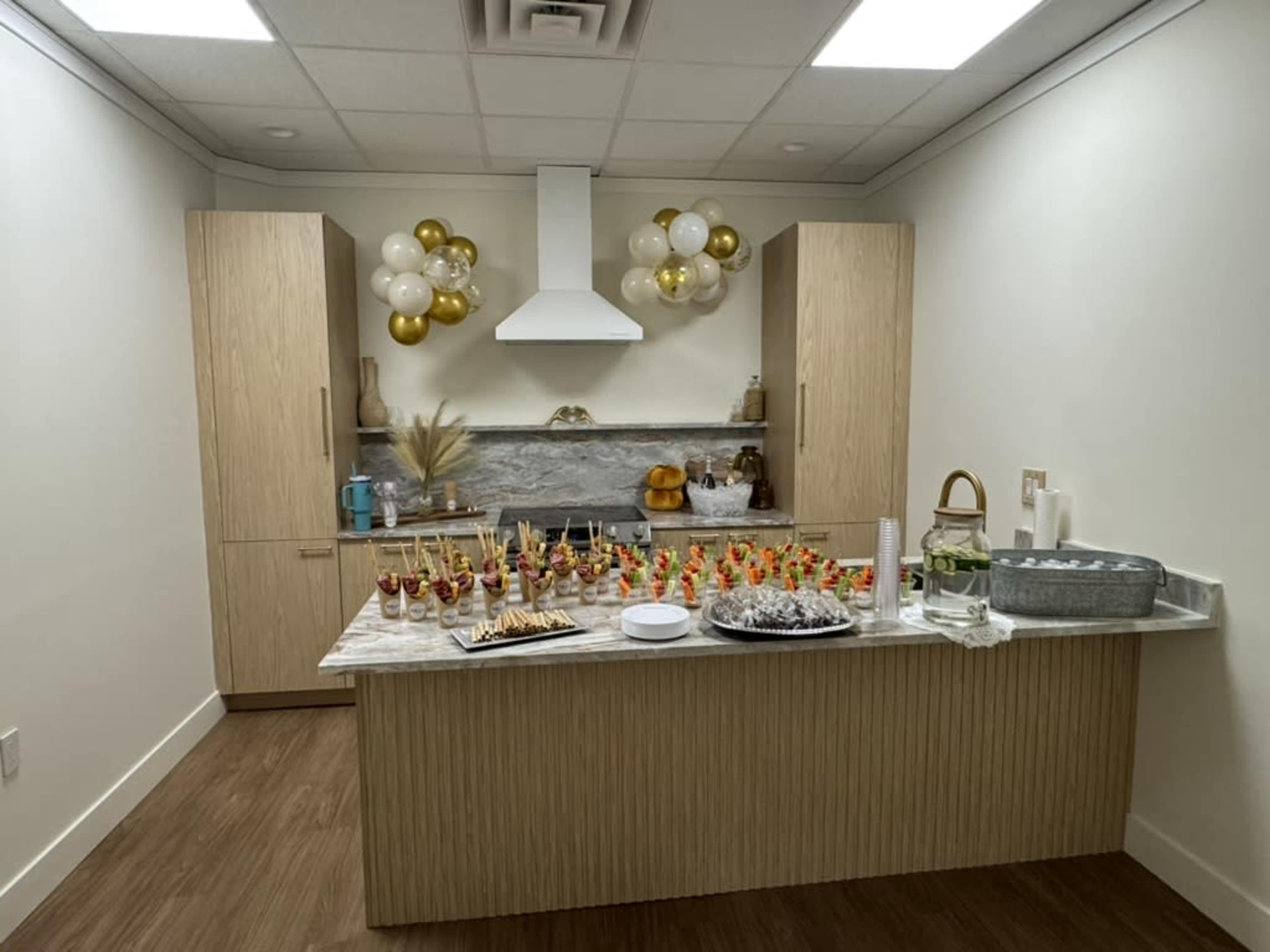The image shows a decorated kitchen space with a table featuring an array of appetizers and beverages, surrounded by festive balloons and autumn-themed decorations.
