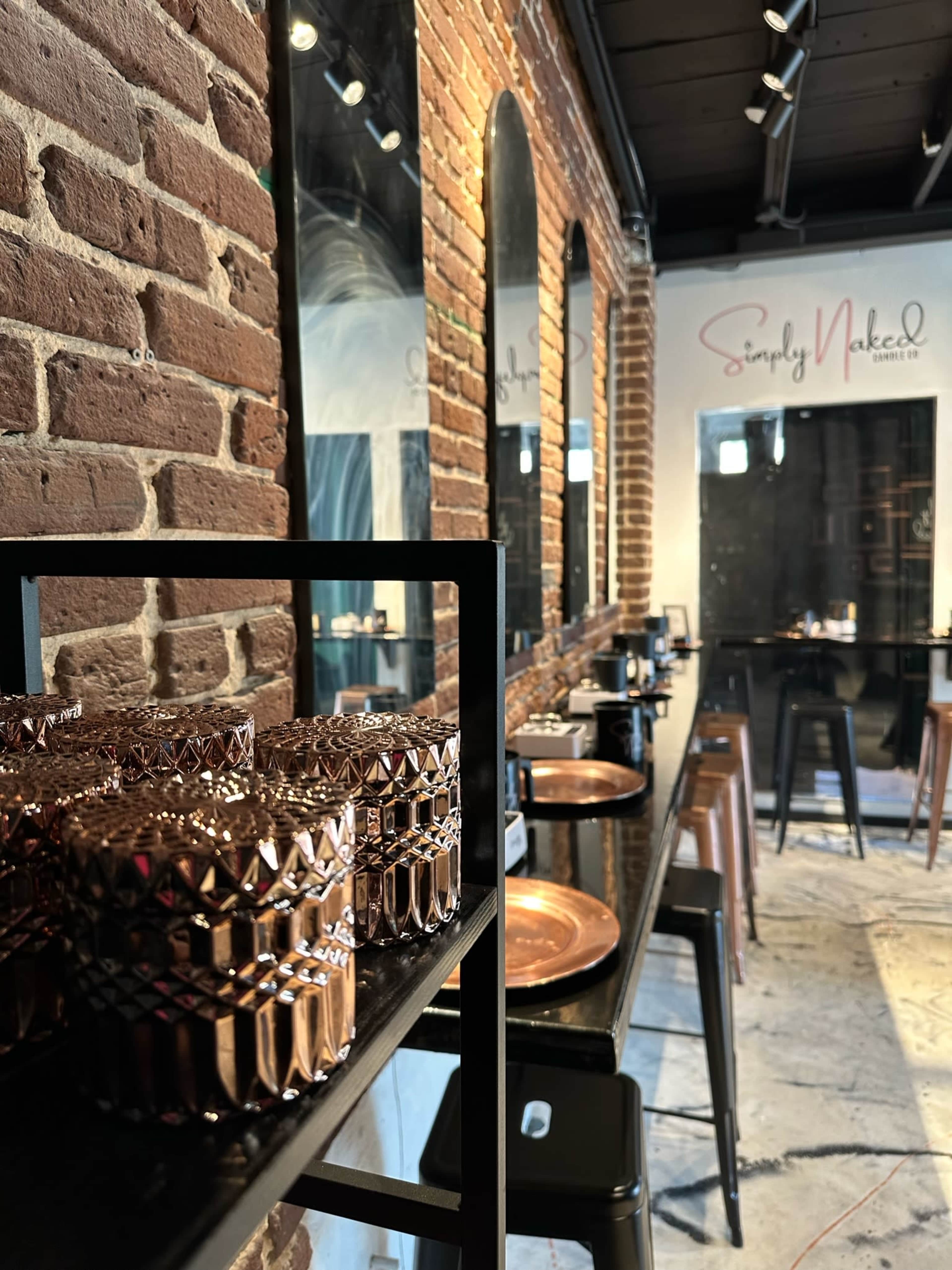A modern interior features a brick wall, black shelving with decorative glassware, and a row of high stools along a counter.