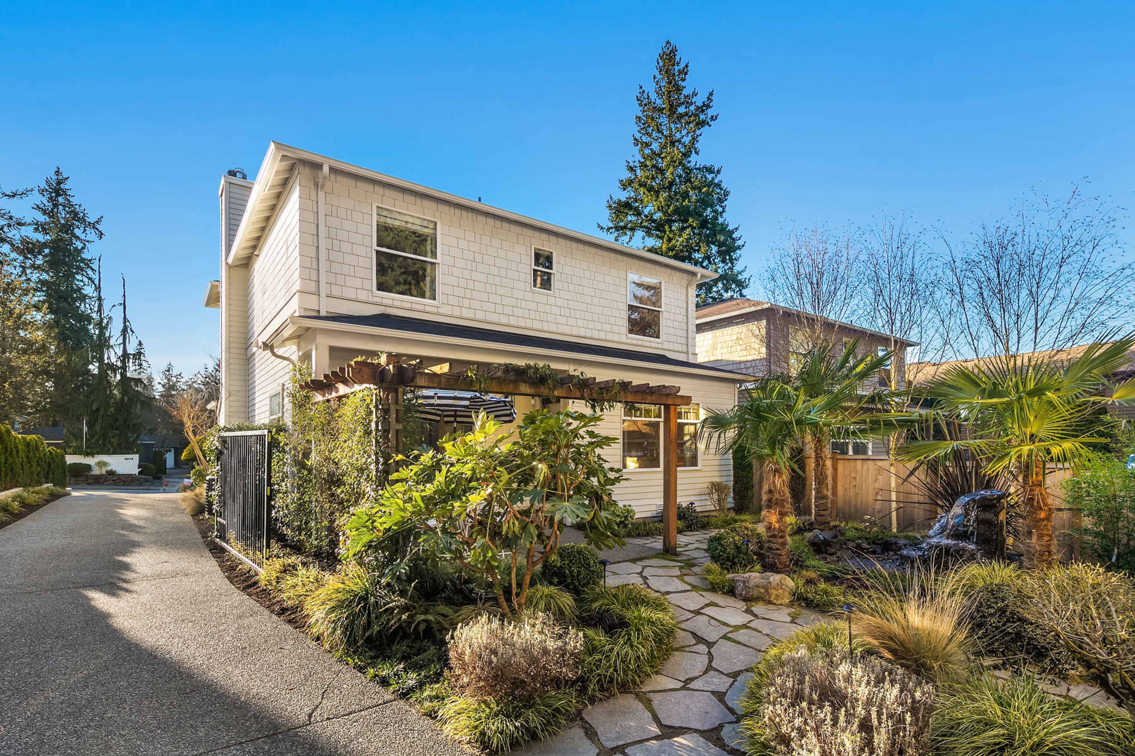 A two-story house with a landscaped front yard and stone pathway is situated along a quiet residential street.