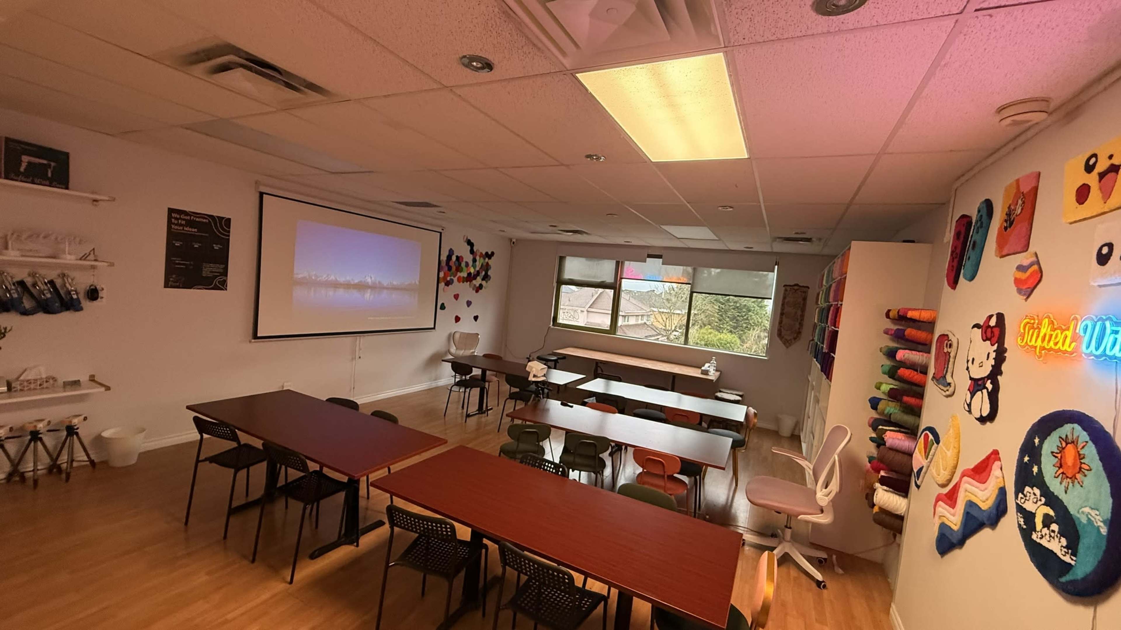 The image shows a classroom with multiple tables and chairs arranged for seating, a projector screen at the front, and colorful decorations on the walls.