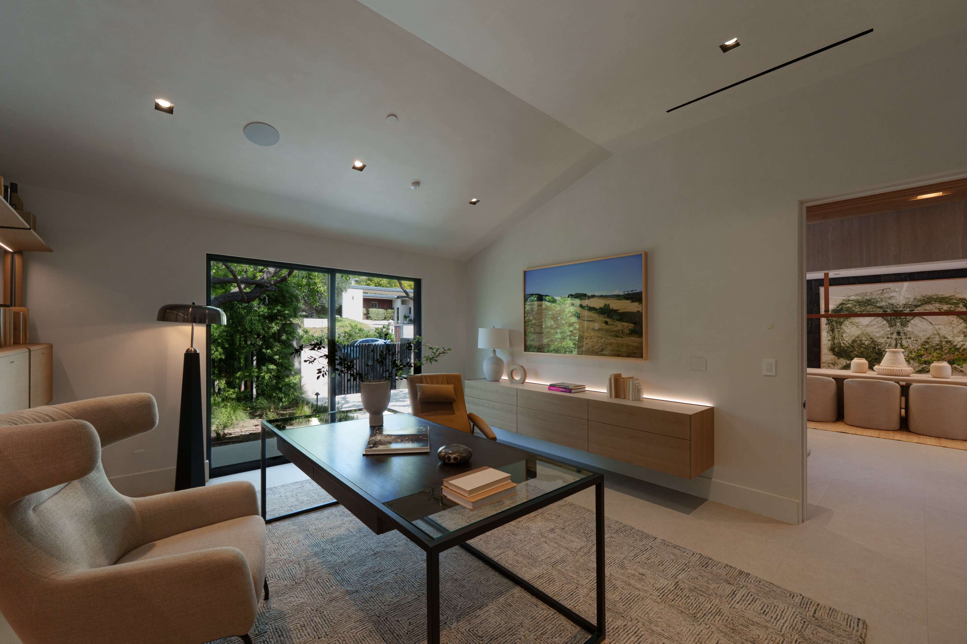 A modern home office features a sleek desk, comfortable chair, and large windows overlooking a garden.