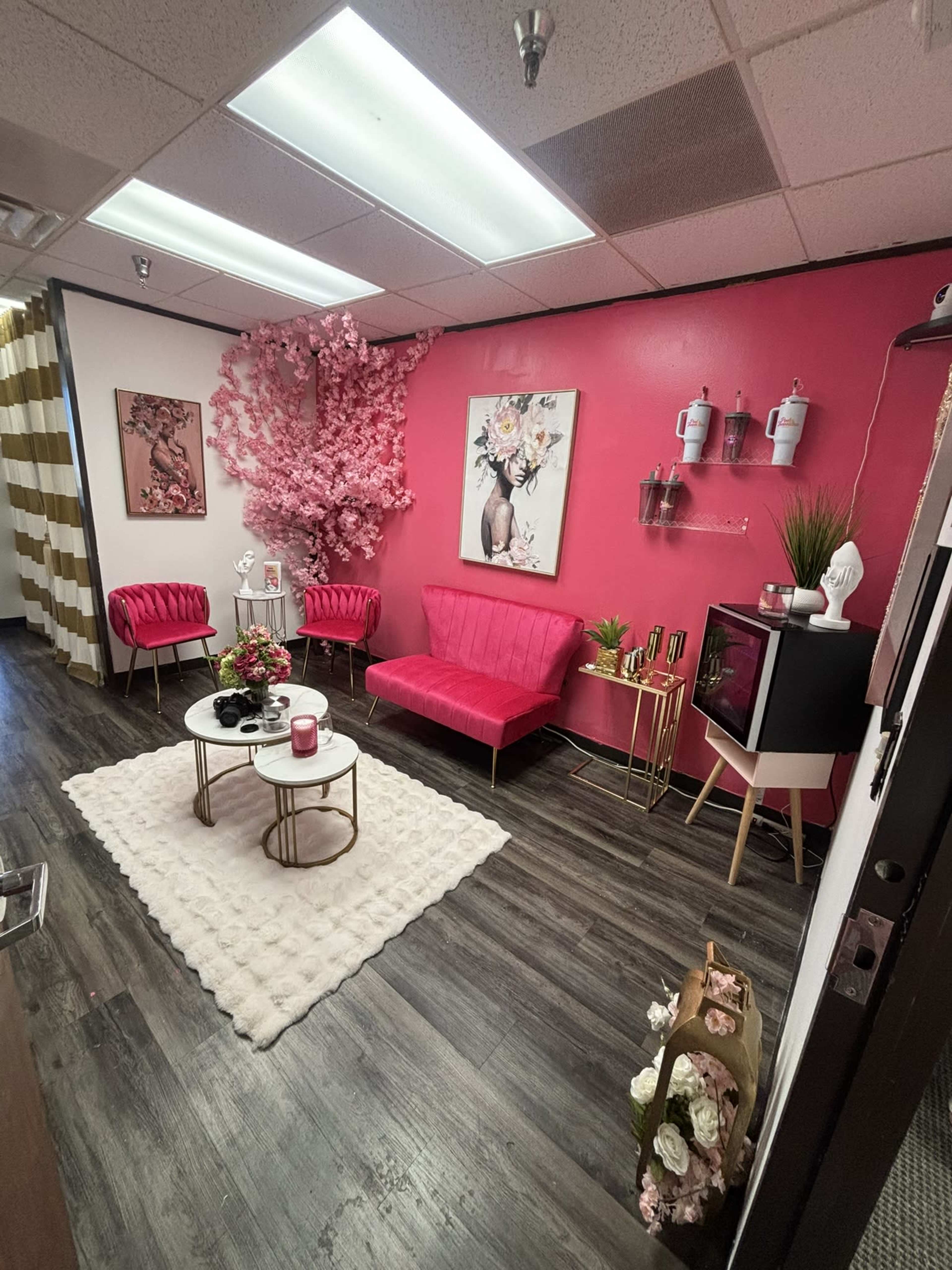 The image shows a brightly colored salon or spa reception area with pink walls, decorative flowers, seating, and a coffee table.