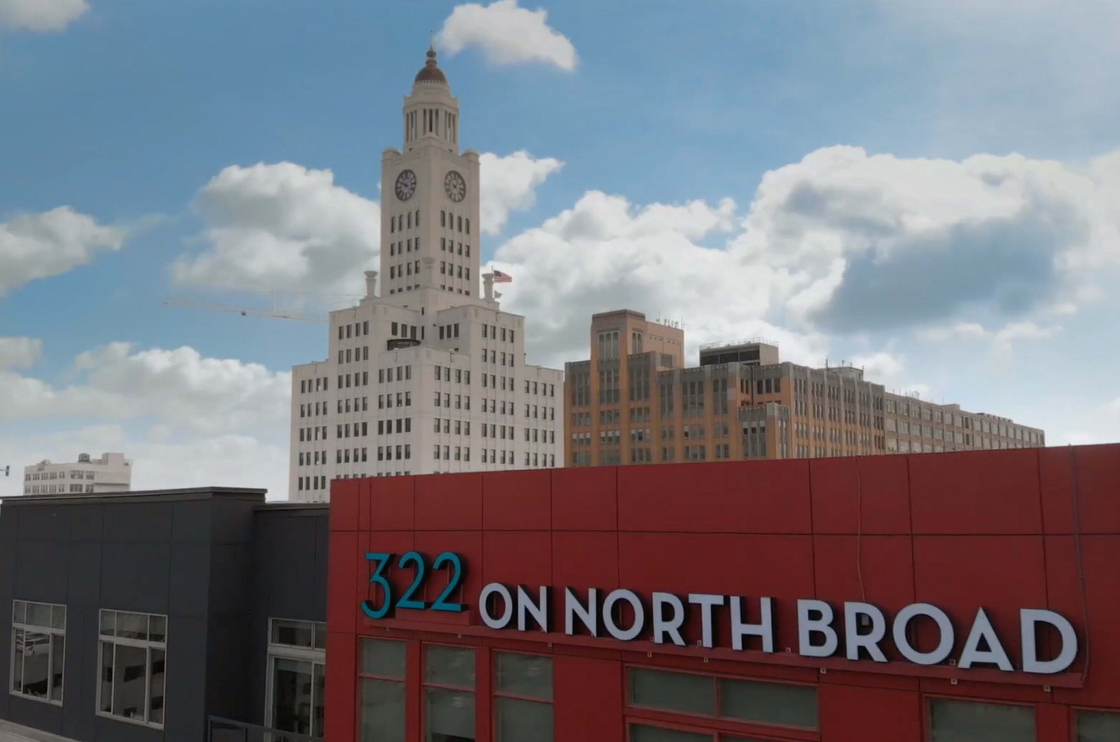 The image shows a building with a red facade labeled "322 ON NORTH BROAD" in the foreground, with a tall, historic clock tower building in the background under a partly cloudy sky.
