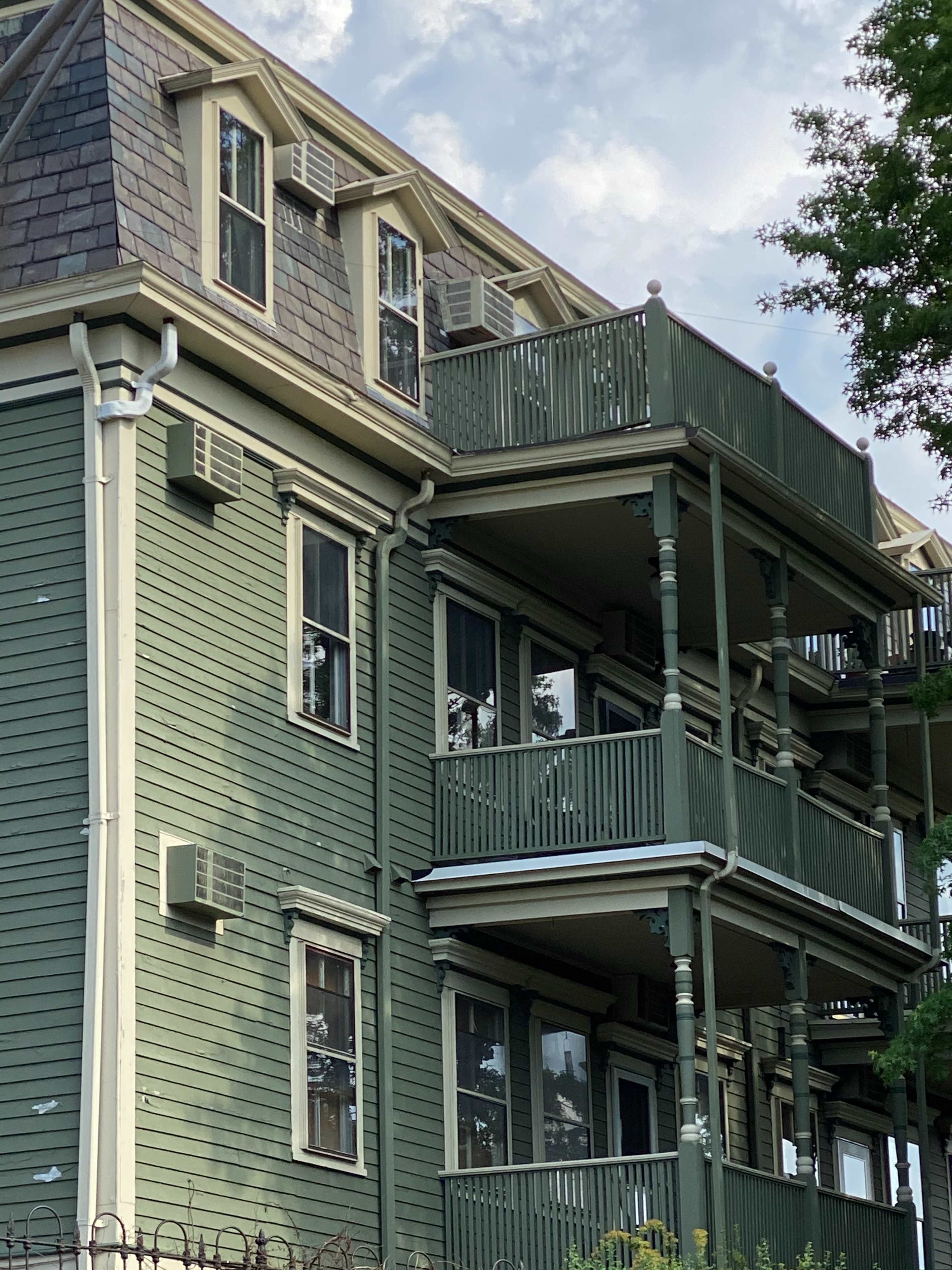 A multi-story green wooden building with multiple balconies and air conditioning units.