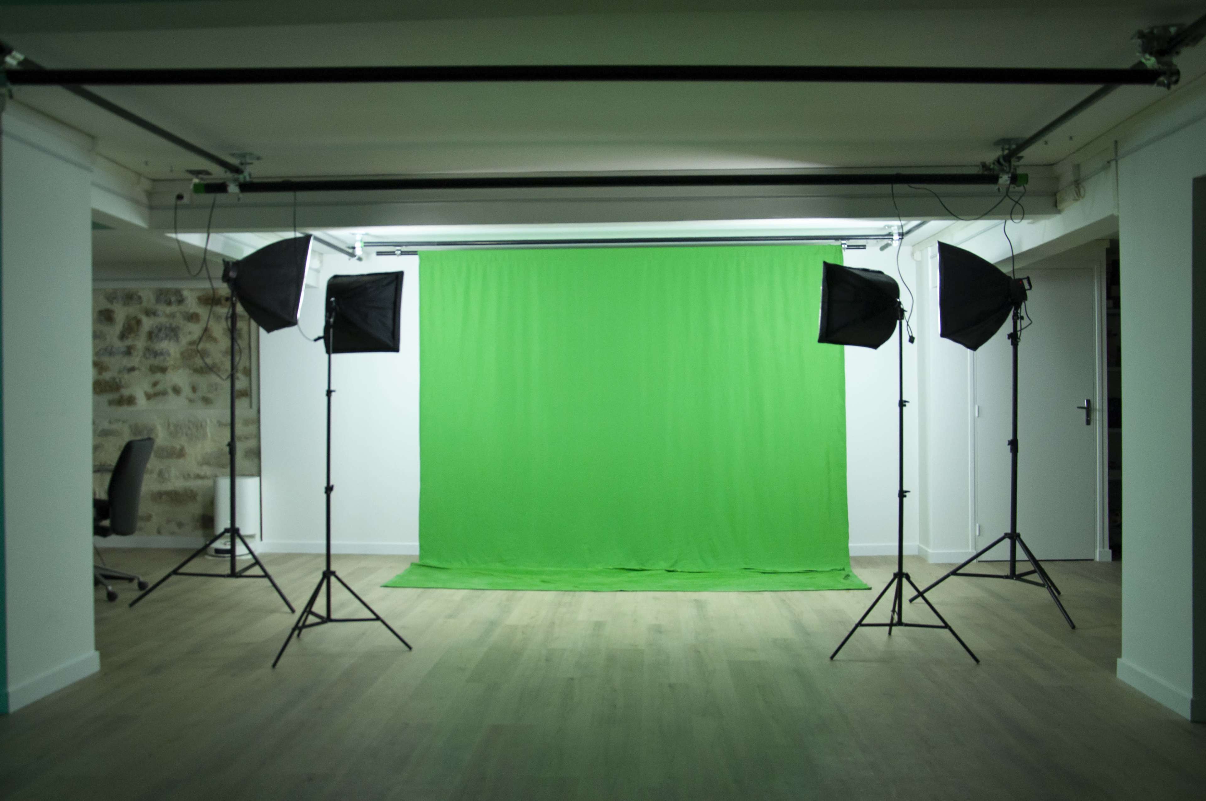 A photo studio equipped with a green backdrop and four lighting setups.