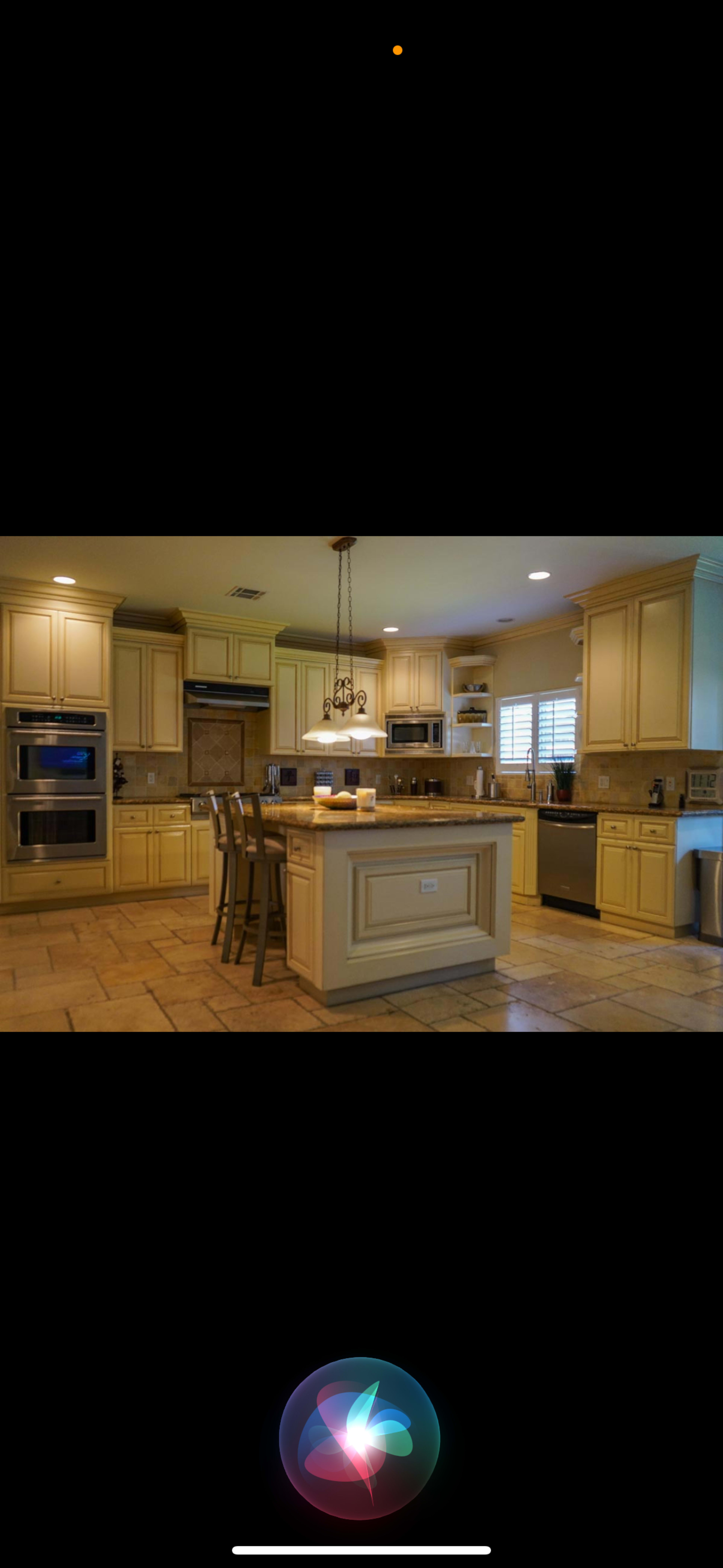 A spacious kitchen features light-colored cabinets, a large island with four chairs, and modern appliances.