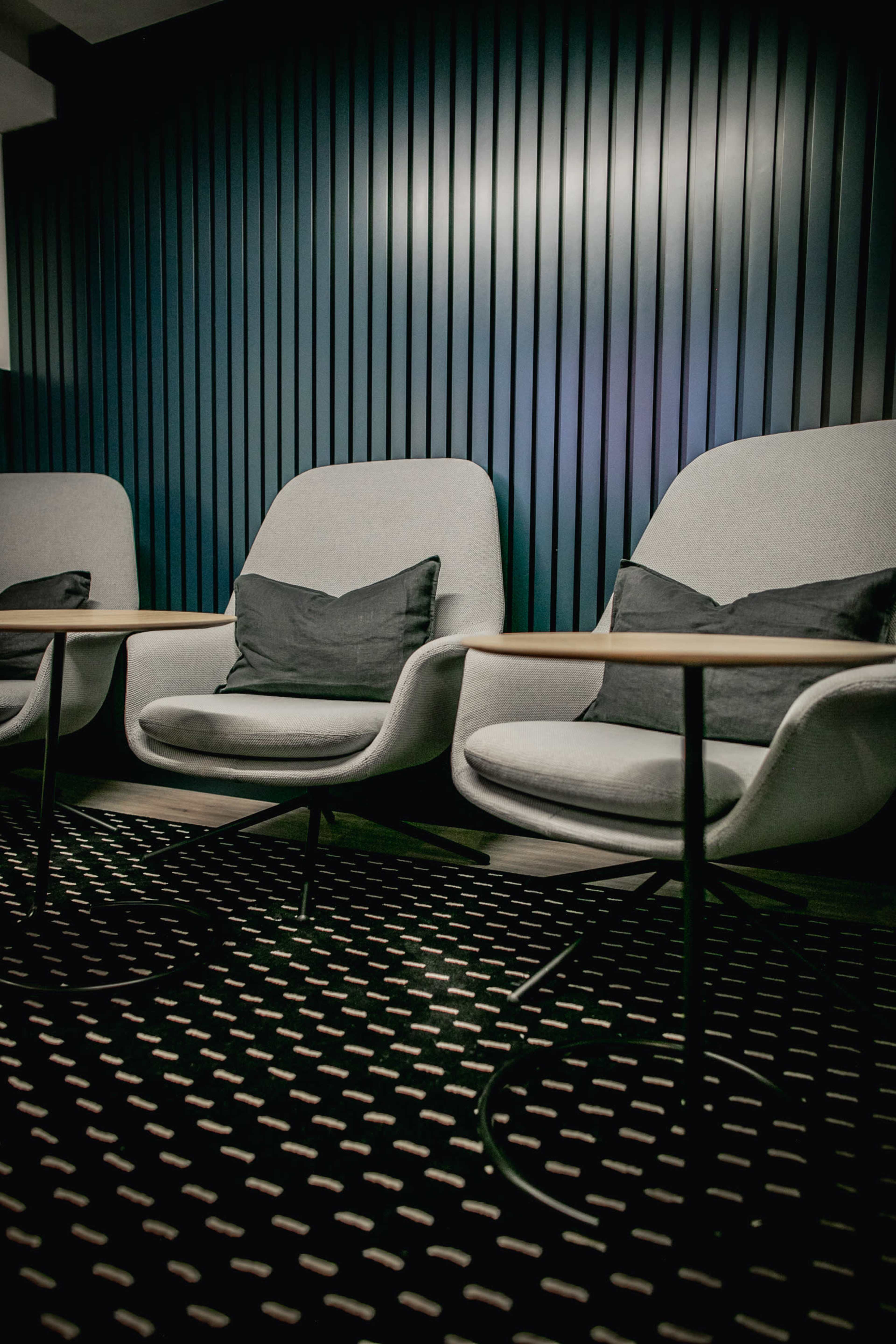 Two gray chairs with cushions are positioned in front of a wooden table, set against a striped dark wall.
