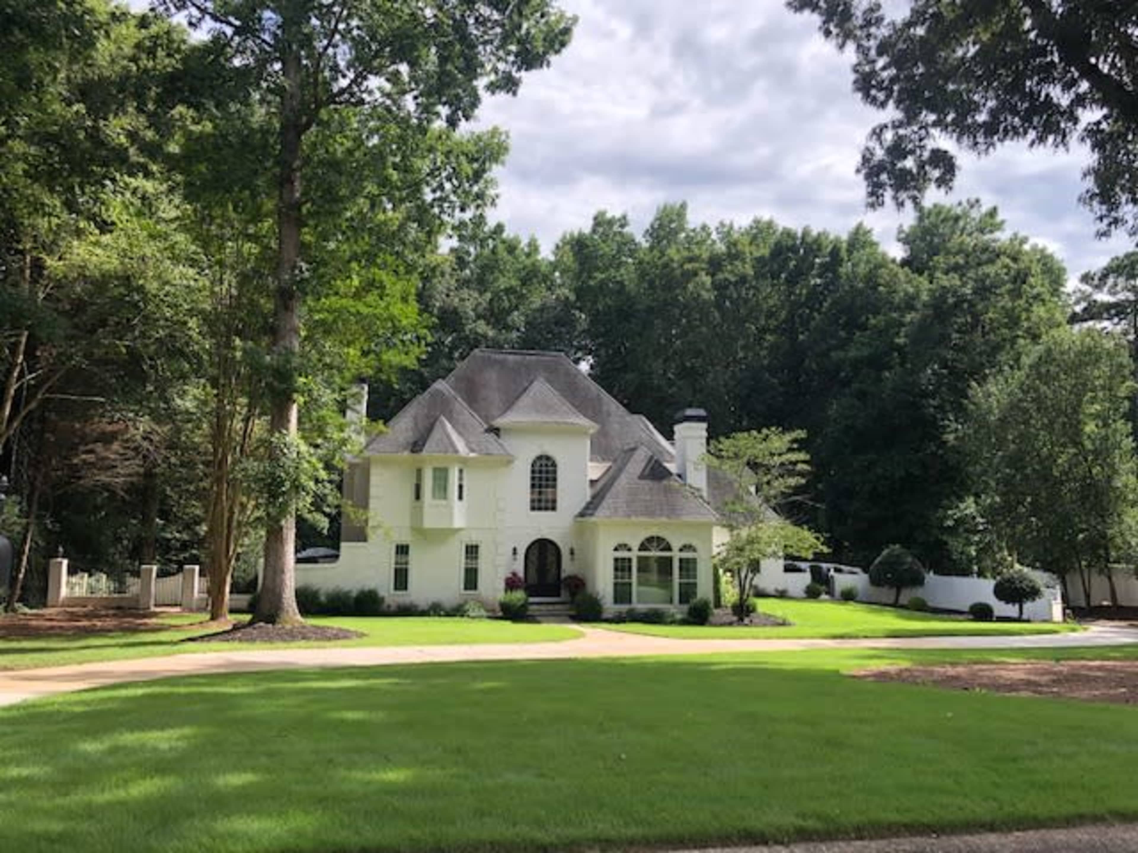 A large white house with a gray roof is set among tall trees and manicured lawns.