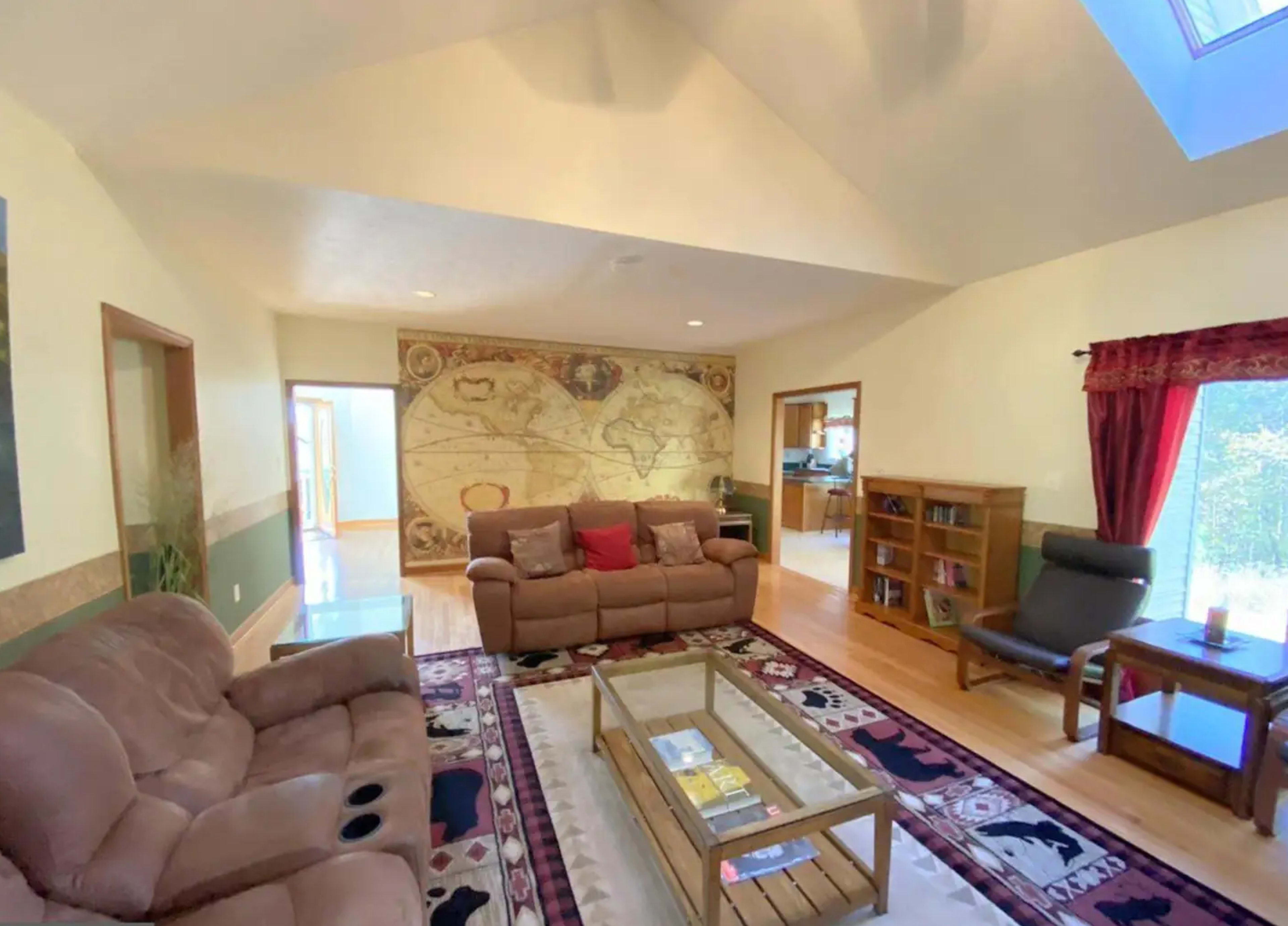 The room features a pair of brown sofas, a coffee table, and a large world map mural on the wall, with large windows allowing natural light to enter.
