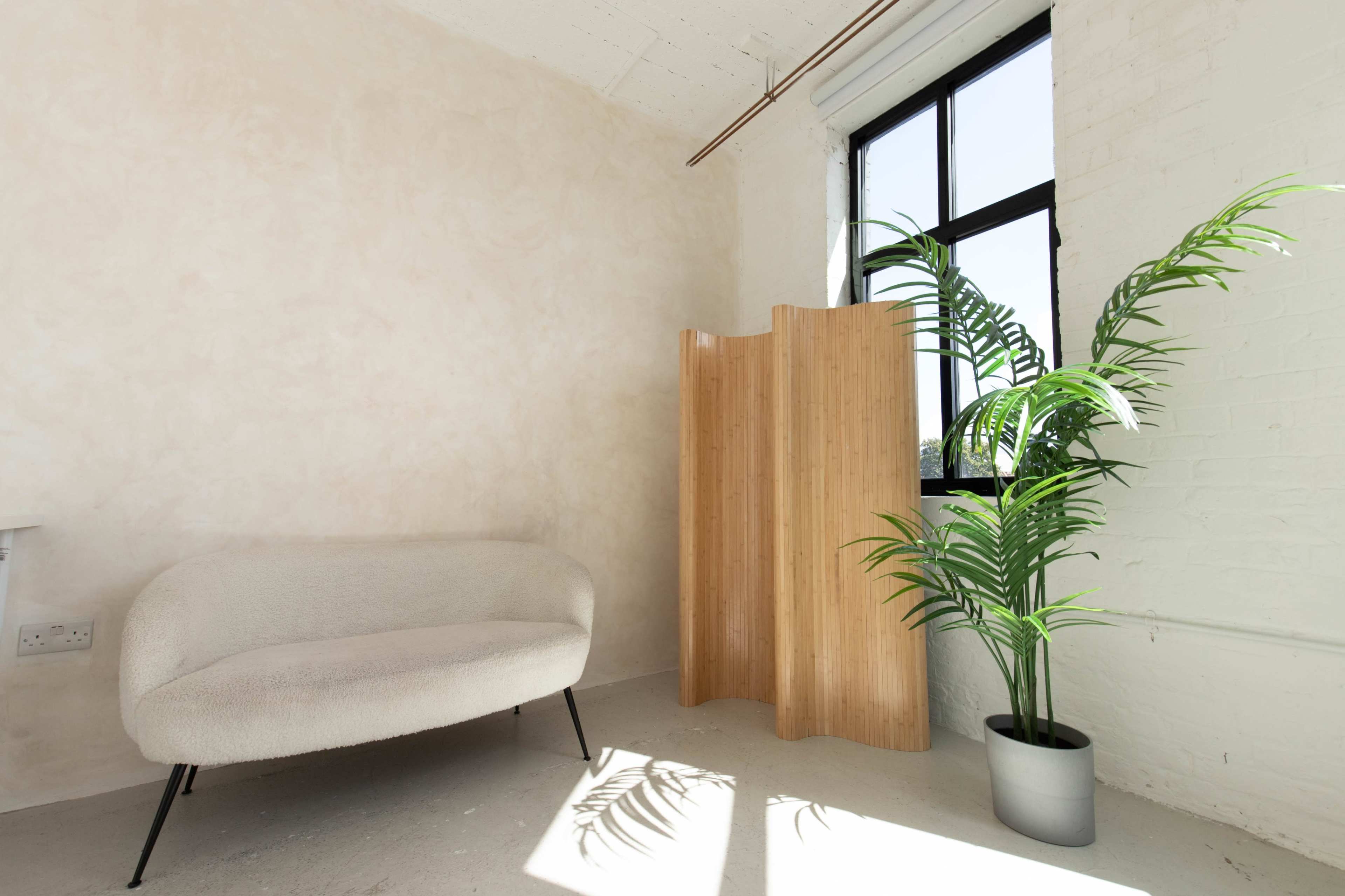 A light-filled room featuring a curved sofa, a wooden folding screen, and a potted plant next to a large window.