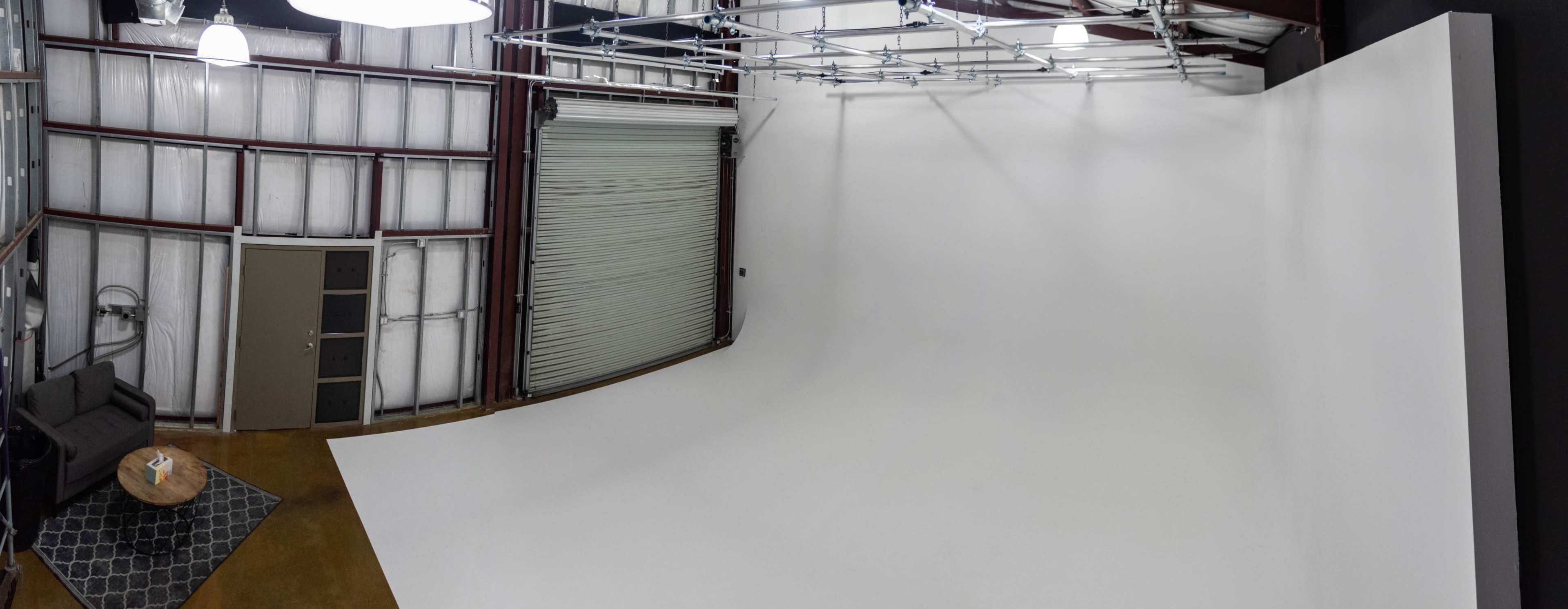 A spacious studio features a large white backdrop and a seating area with a coffee table.