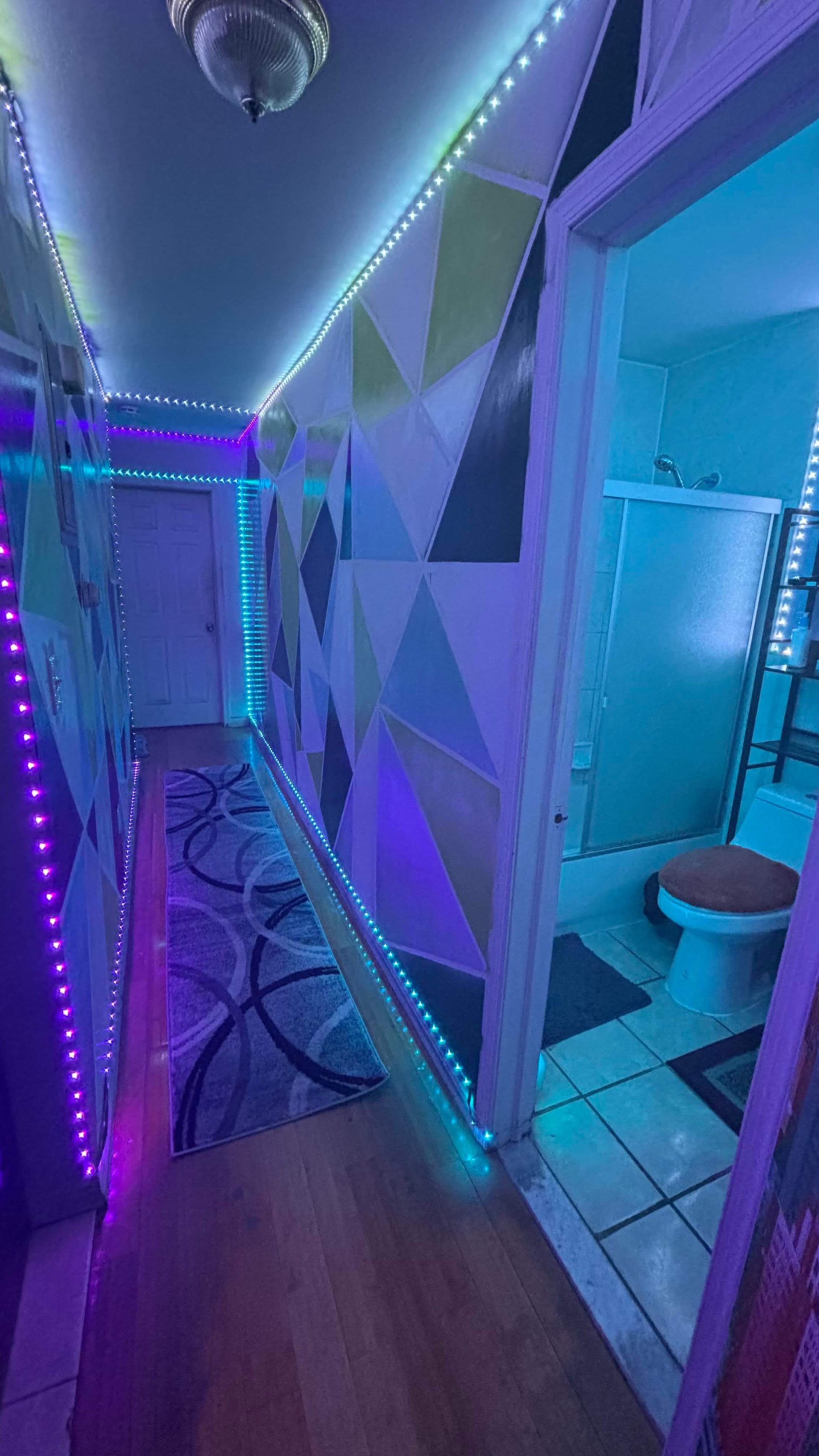 The image shows a brightly colored hallway with geometric wall designs and LED light strips illuminating the edges.