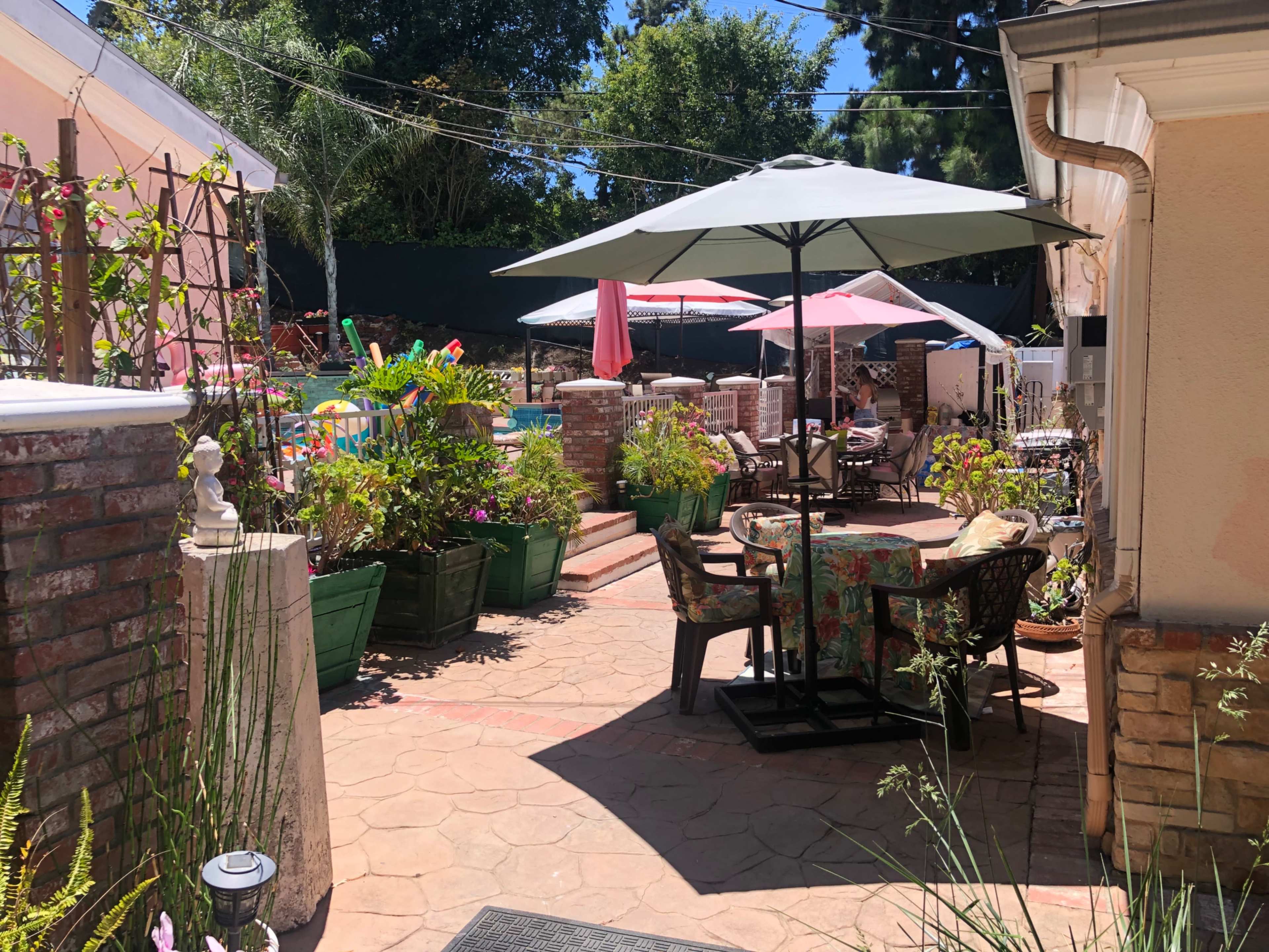 A landscaped backyard with colorful plants, patio furniture, and two umbrellas providing shade.
