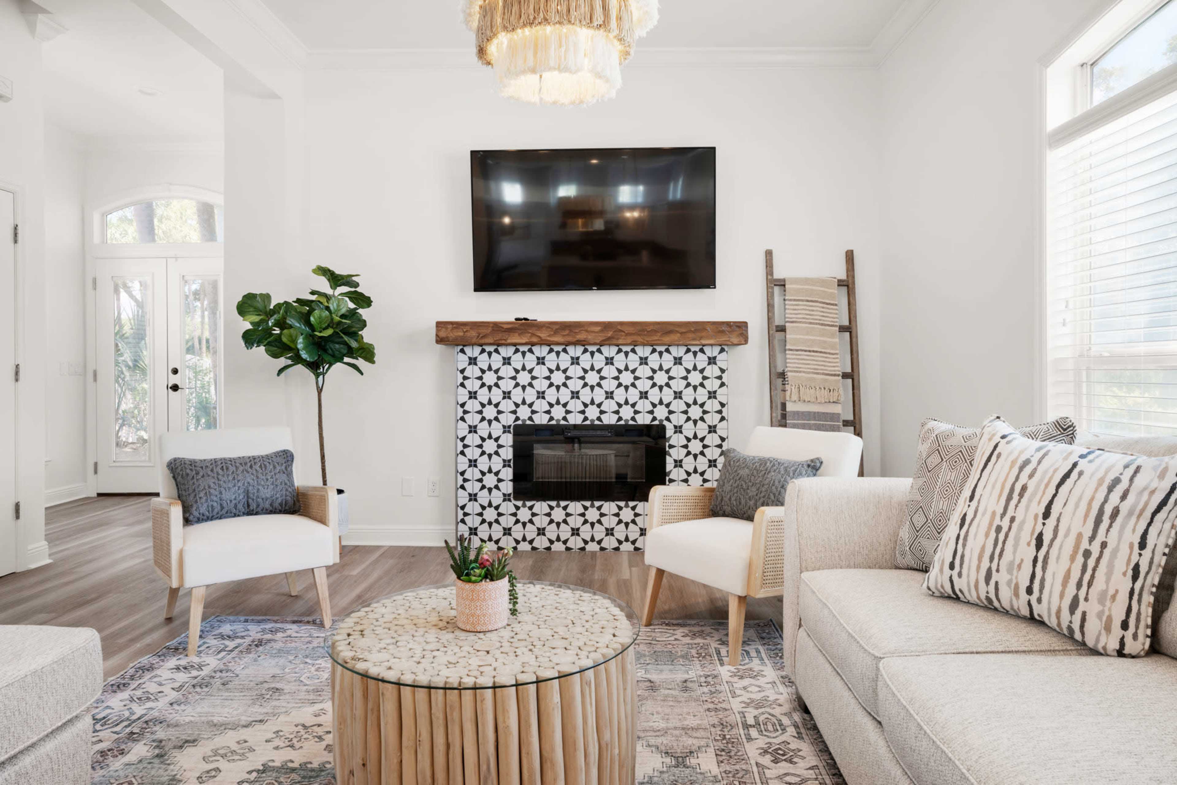 The scene features a bright living room with a television mounted above a decorative fireplace, surrounded by light-colored furniture and a circular coffee table.
