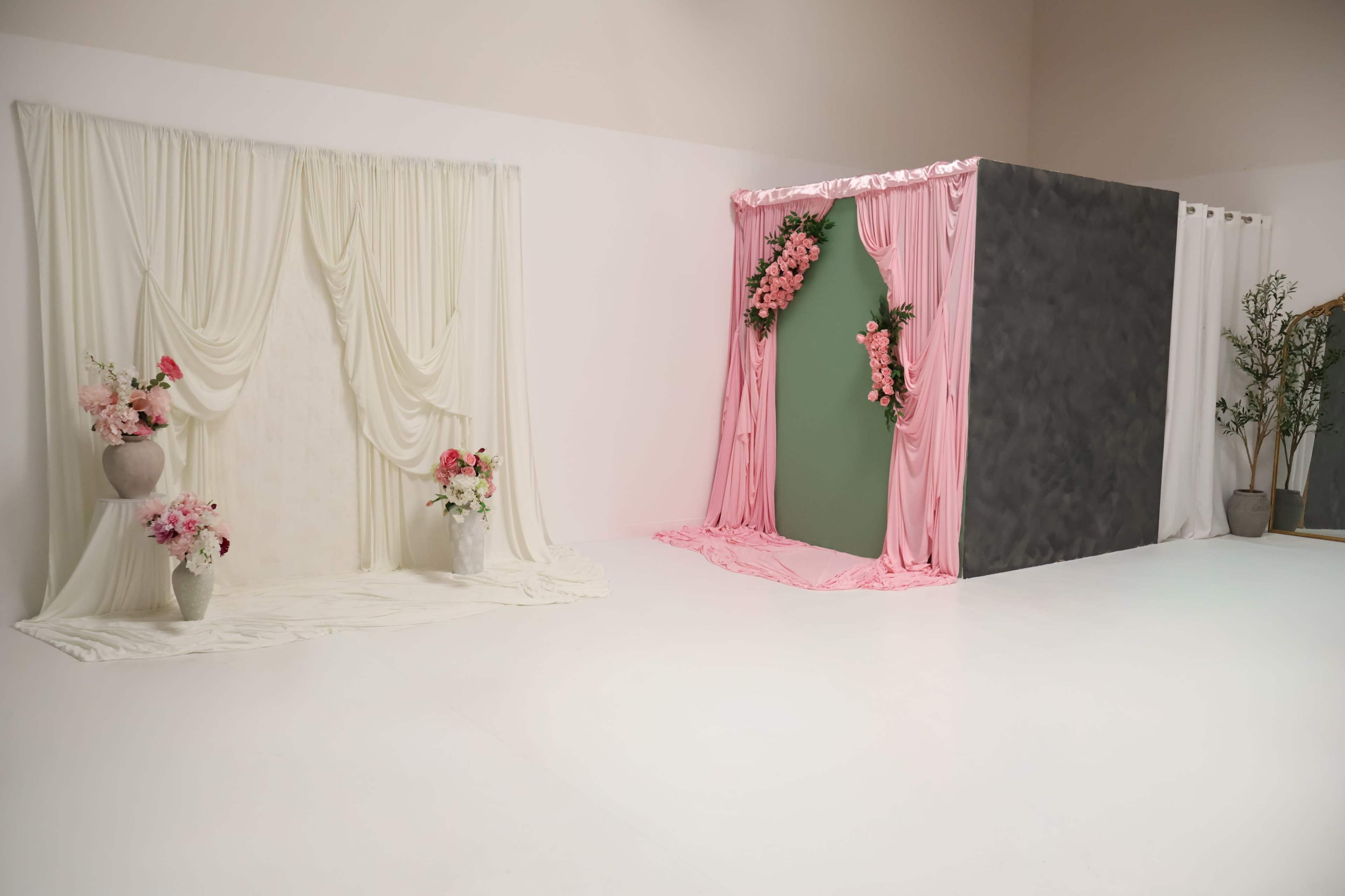 The image features two distinct backdrops in a studio space: one with draped white fabric and flowers, and another with pink fabric decorated with flowers on a gray wall.