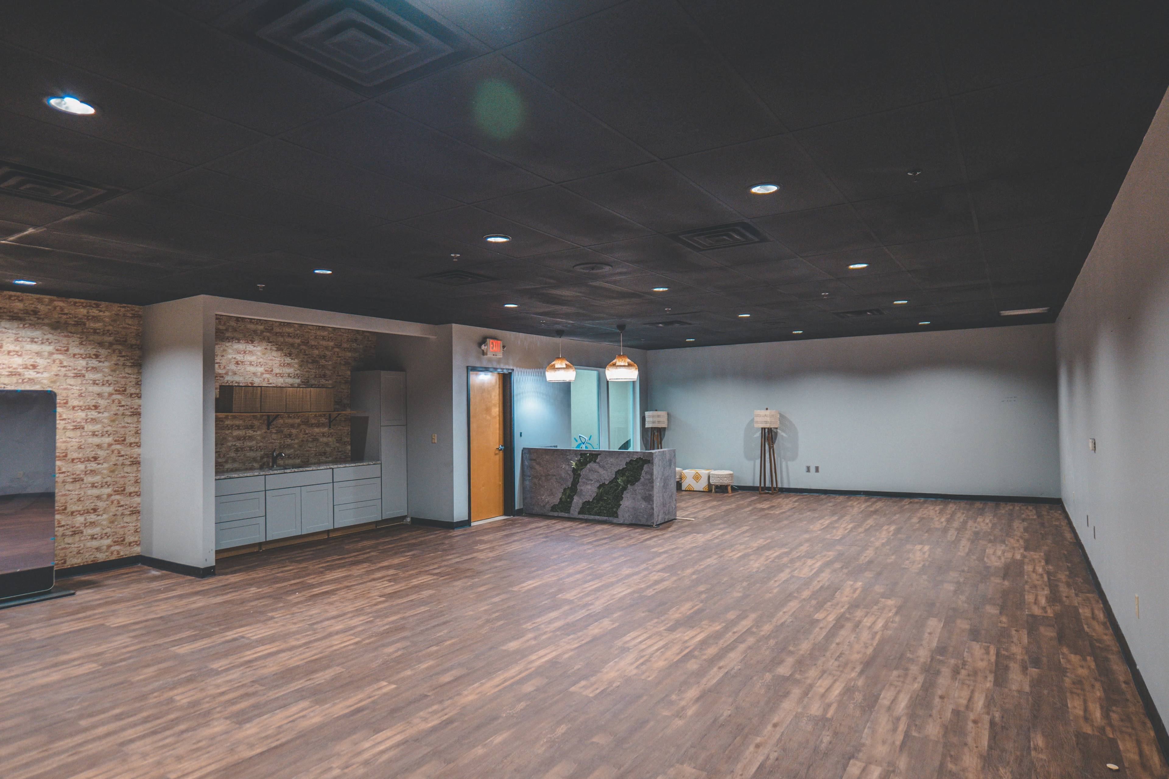 A spacious, empty room with wooden flooring, a kitchenette area, and a reception desk against one wall.