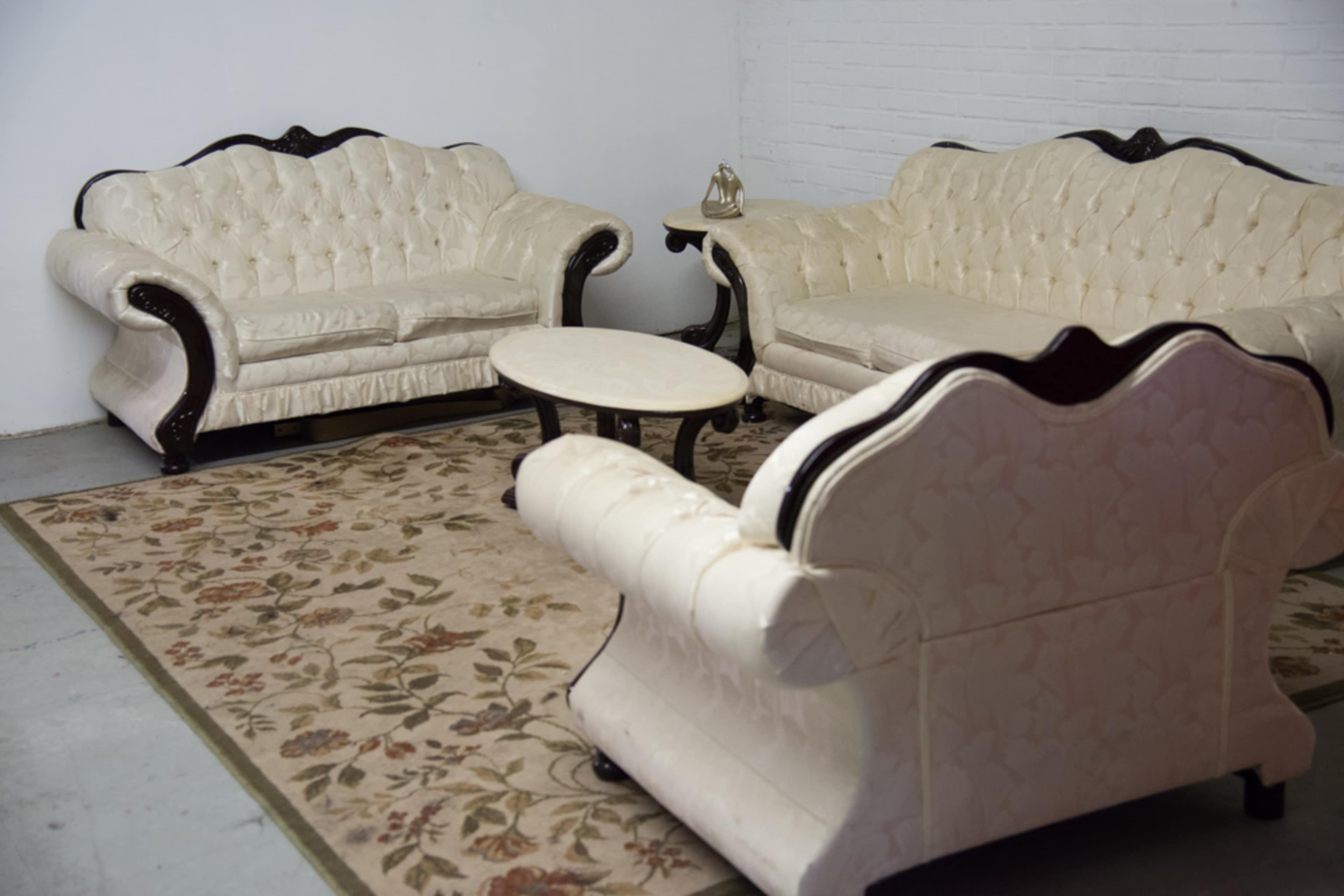 A seating arrangement with two cream-colored sofas and a small round table on a floral-patterned rug in a room with white brick walls.