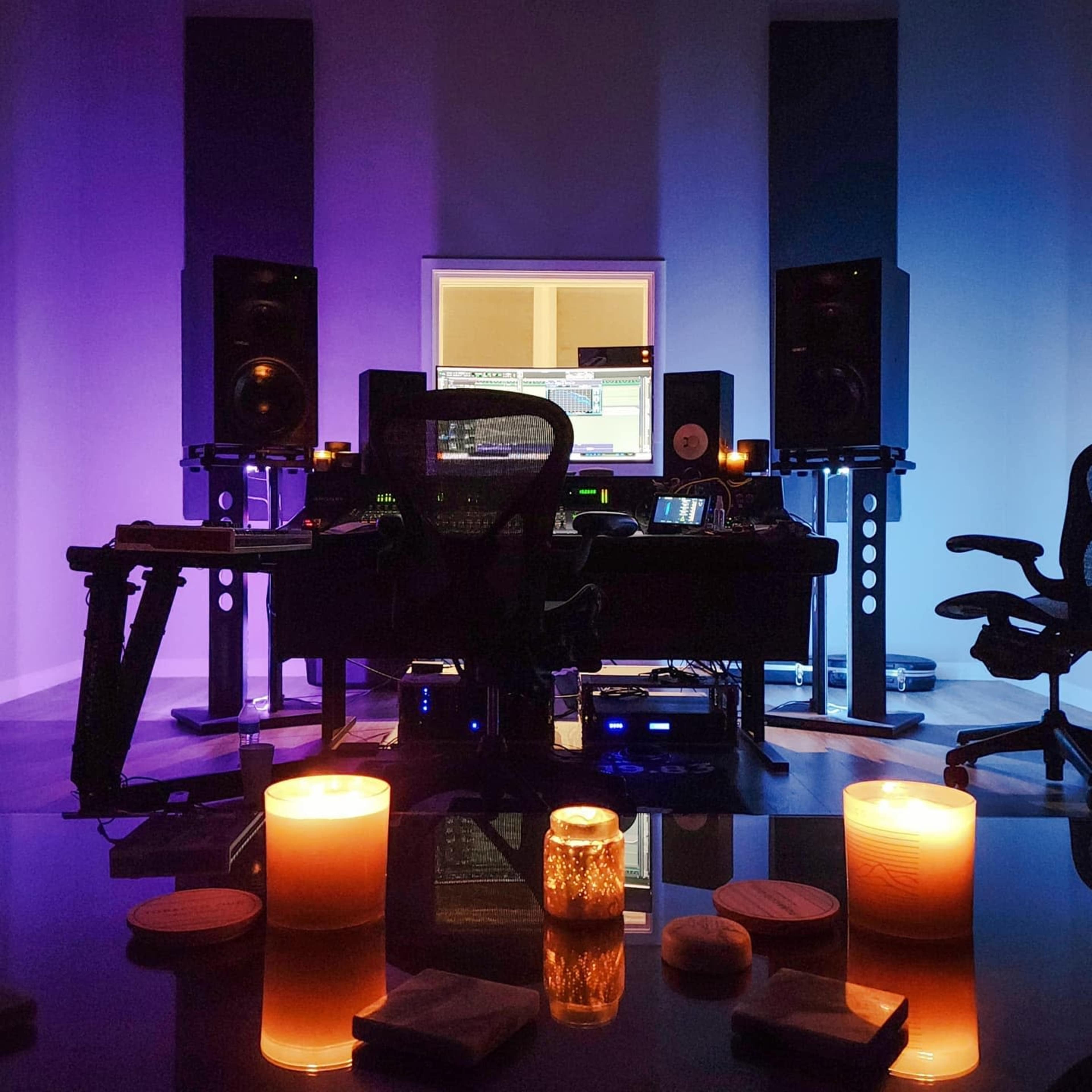 A music studio with a control desk, speakers, and lit candles arranged on a table in the foreground.