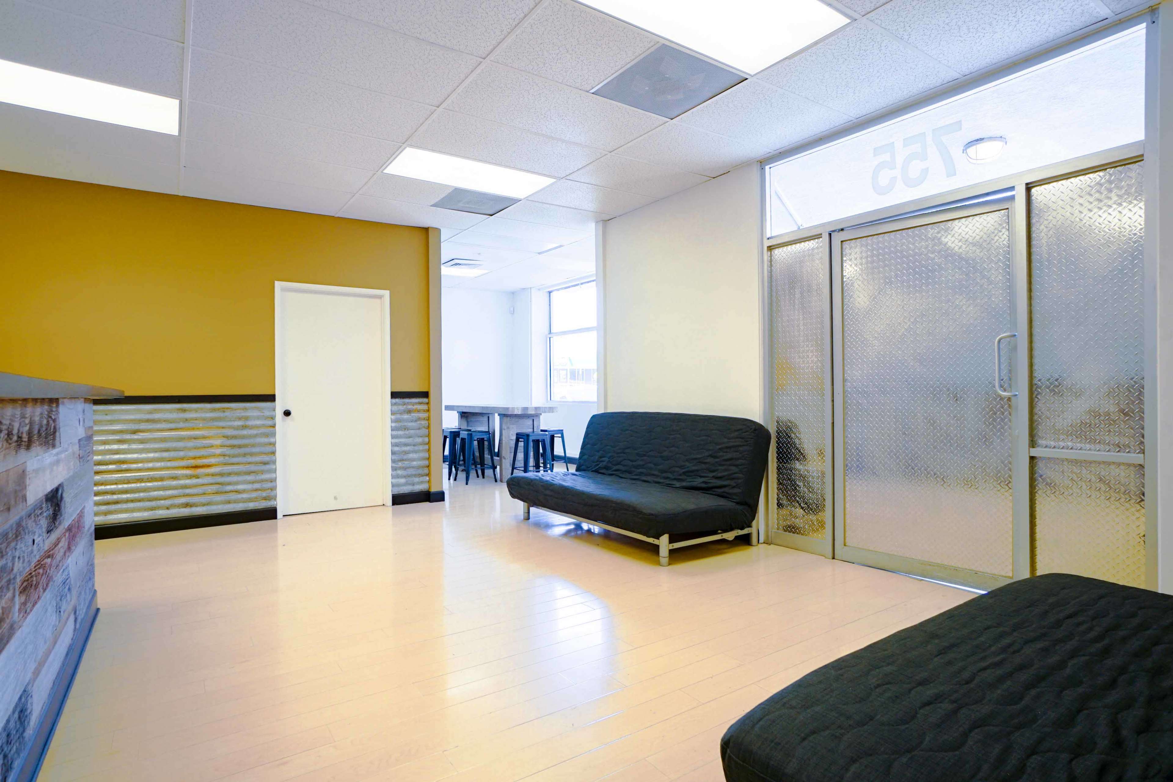An interior space with a reception area featuring a counter, a door, a seating area with black futons, and a large window.