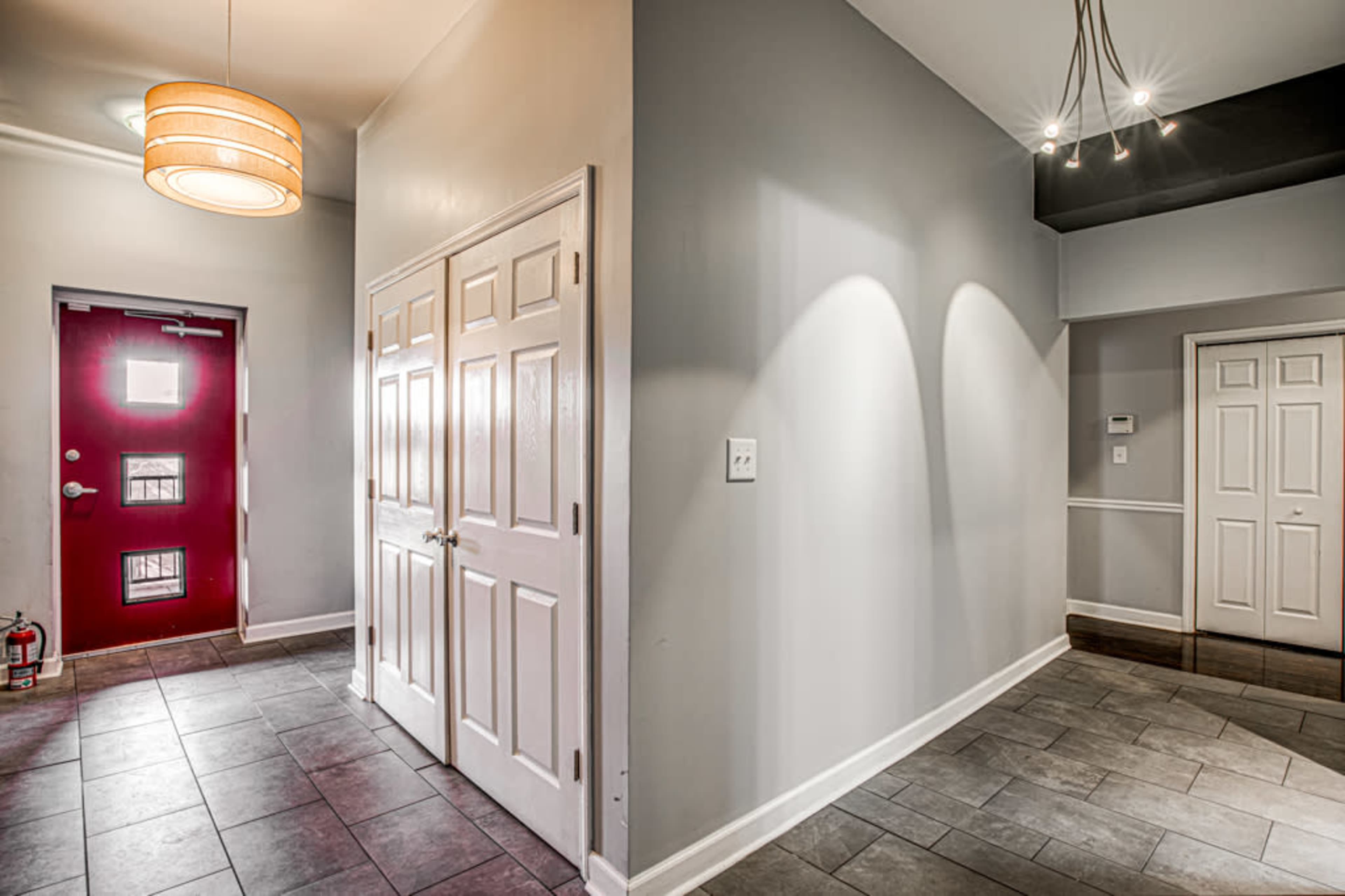 A well-lit entrance hallway with a red door, a closet with double doors, and tiled flooring.