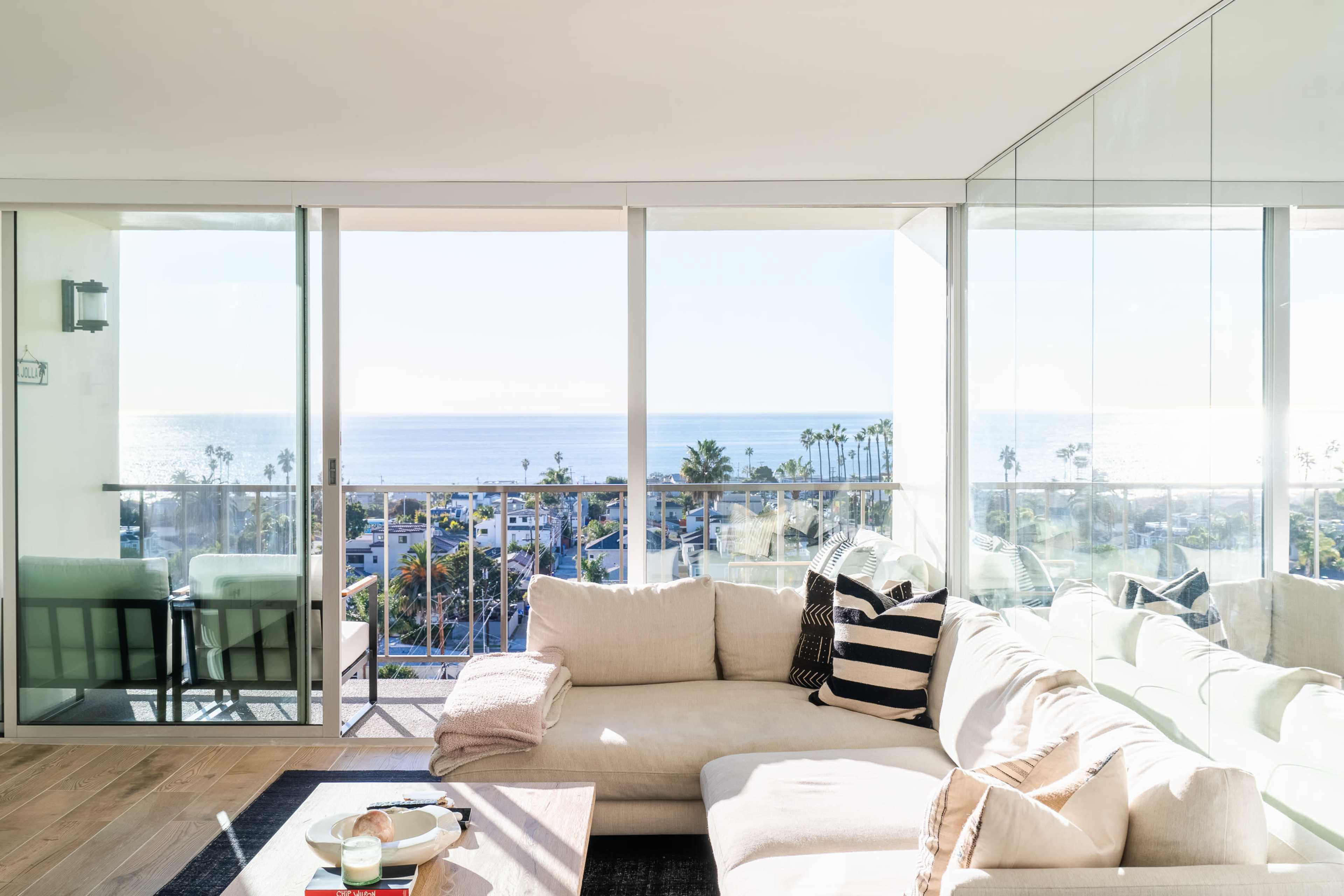 A modern living room with a large sectional couch and a coffee table overlooks a balcony with ocean views.