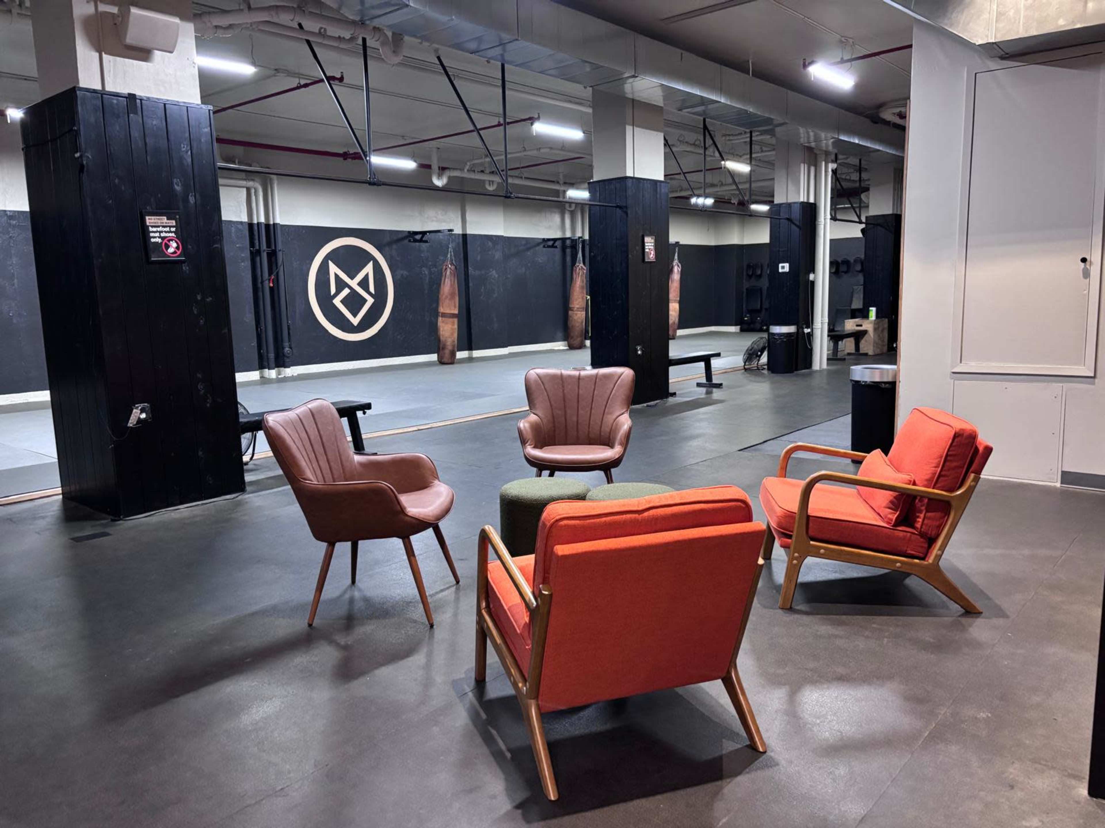 The scene features a fitness studio with a designated training area, equipped with boxing bags and visible workout equipment, surrounded by a lounge area with colorful armchairs.