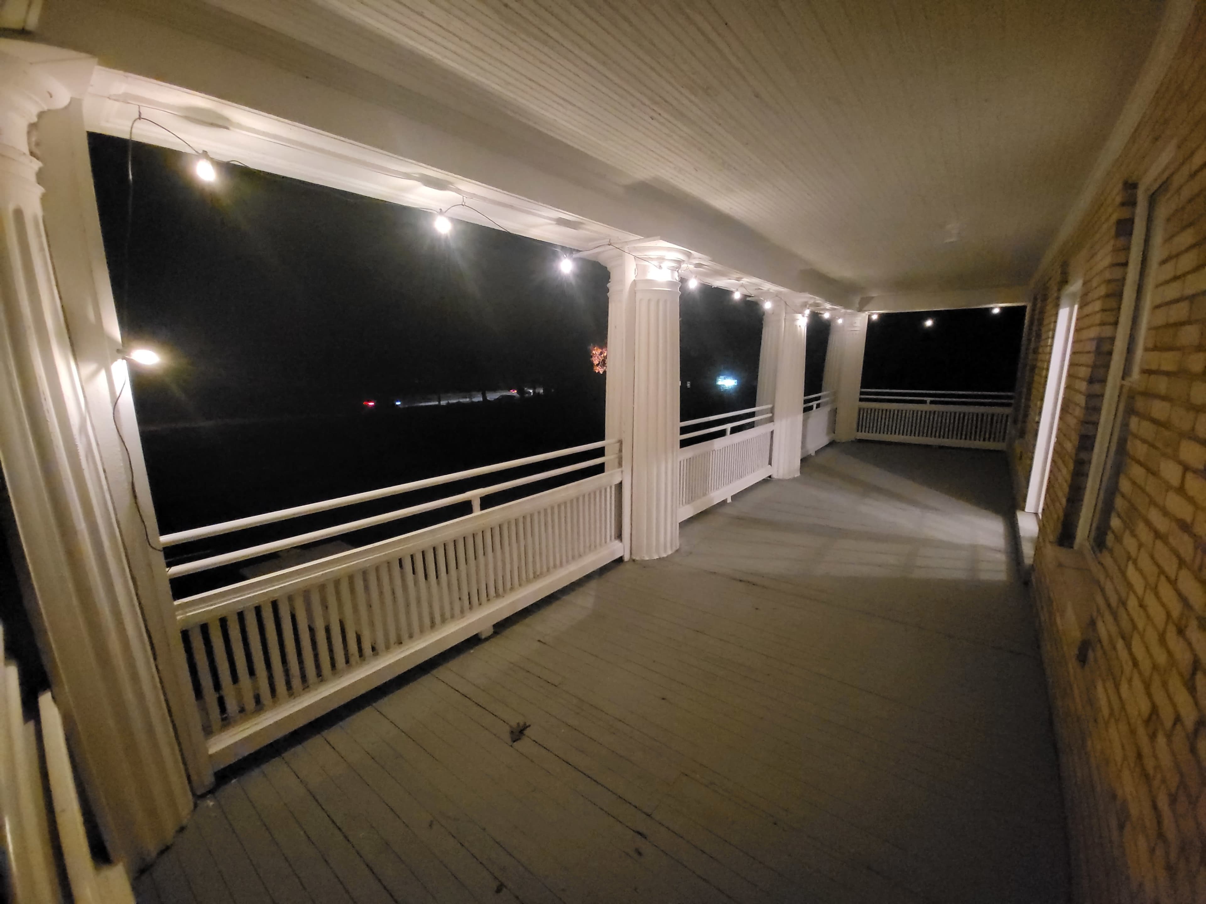 A lit porch at night with white string lights and a view of the dark exterior.