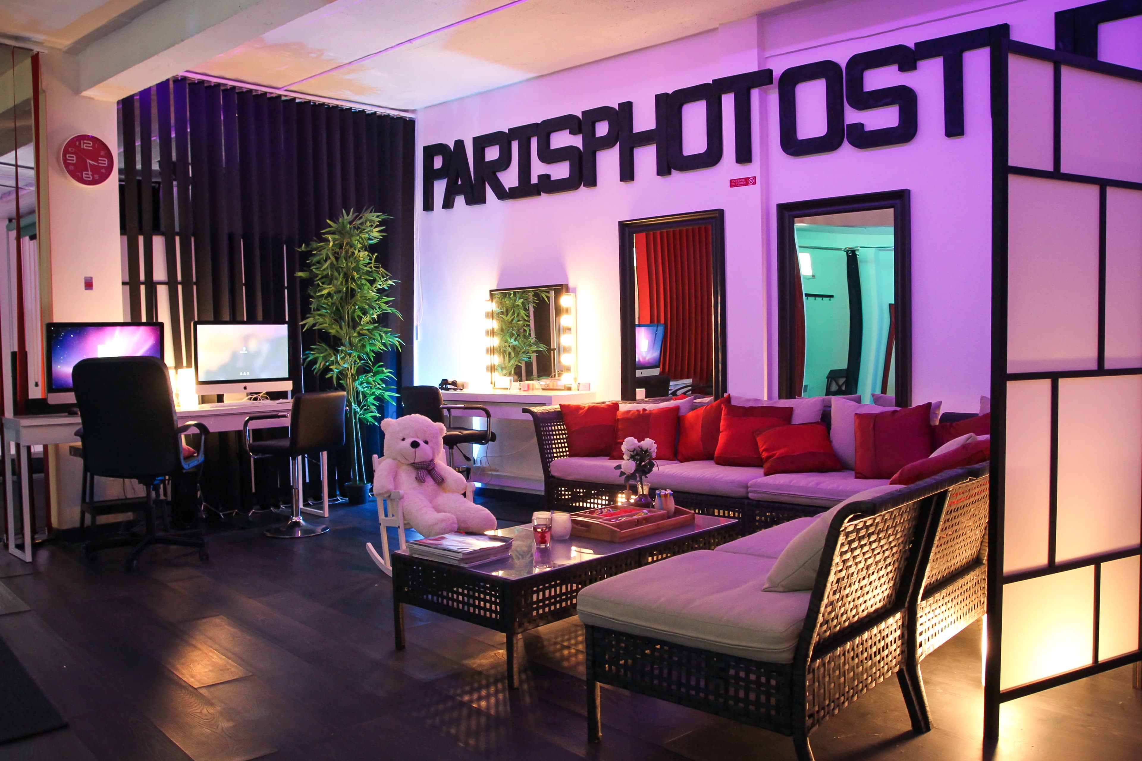 The image shows a modern photography studio with a lounge area featuring a sectional sofa, decorative pillows, and a large sign reading "PARISPHOTOST."