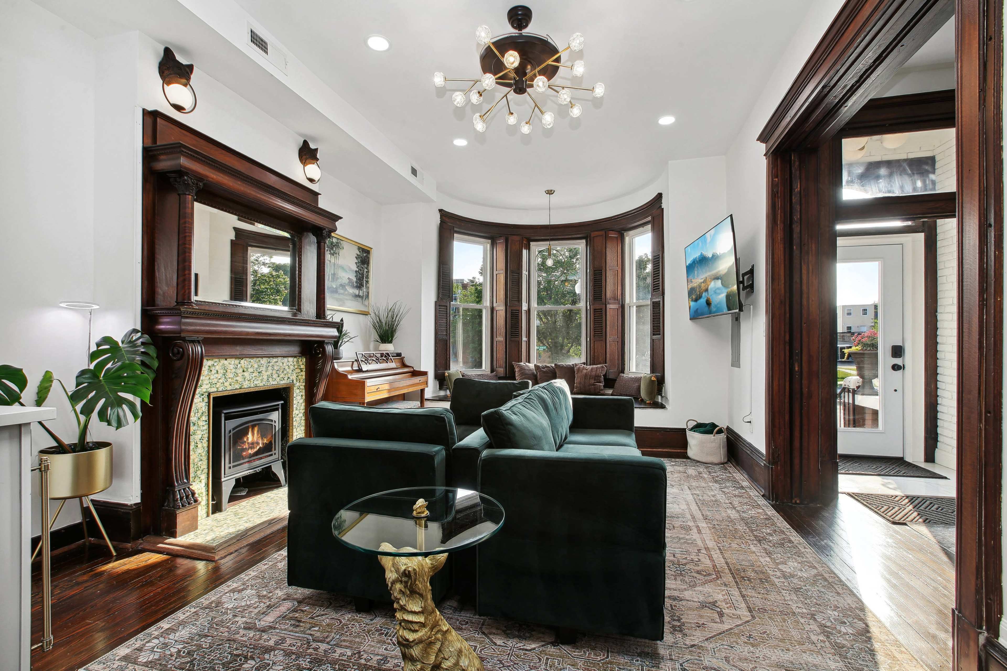 The living room features a modern design with a green sofa, a decorative fireplace, and large windows illuminating the space.