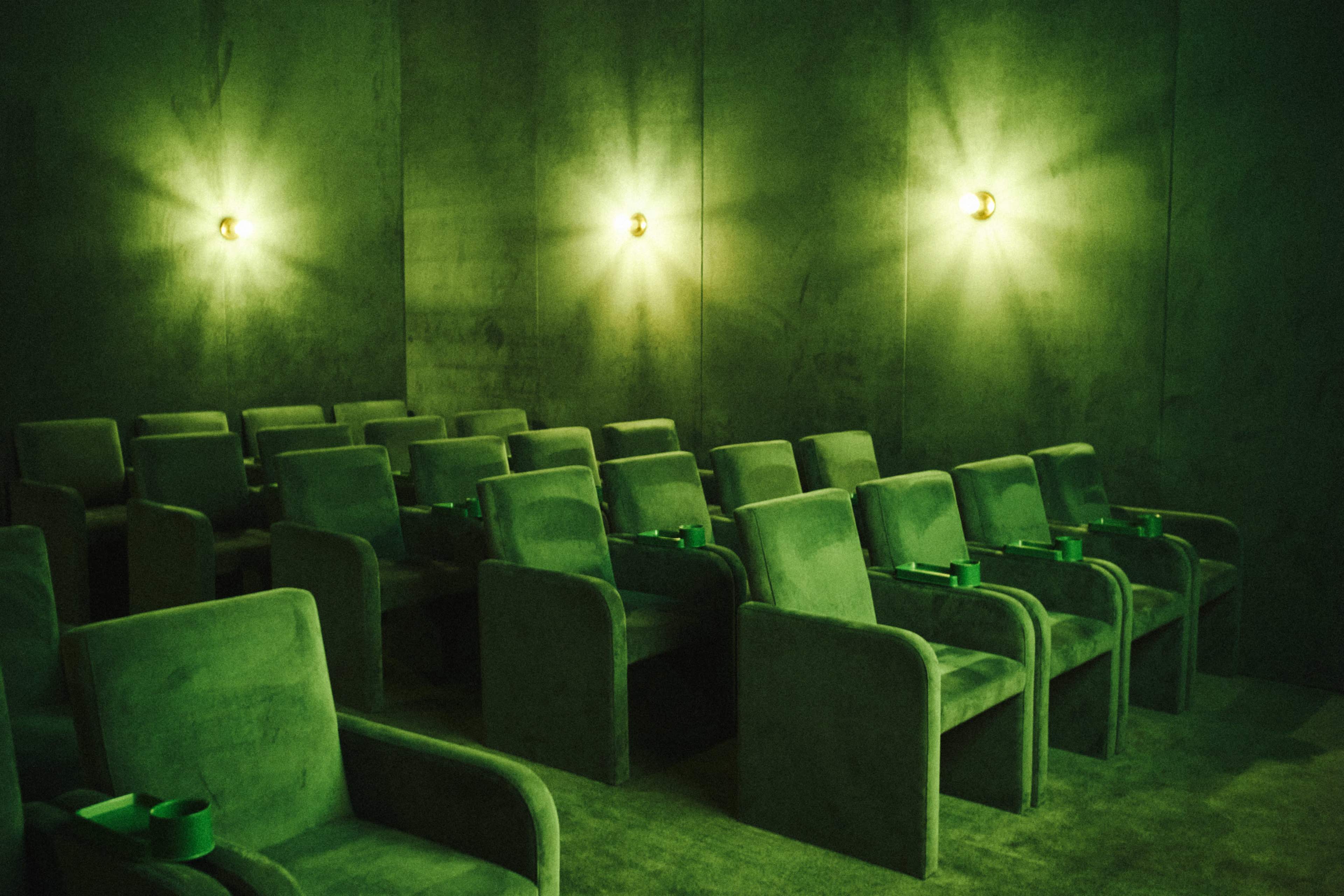 The image shows a dimly lit room with green walls and several green cushioned seats arranged in rows.