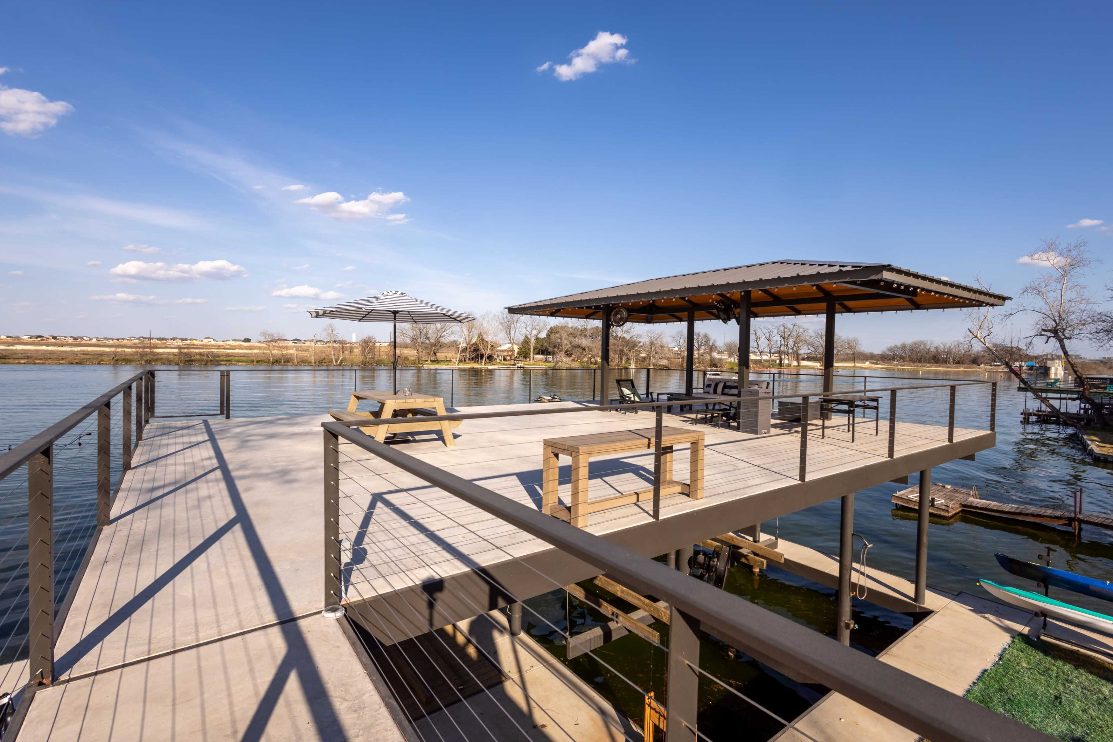 The image shows a waterfront deck with a covered seating area, overlooking a calm body of water.